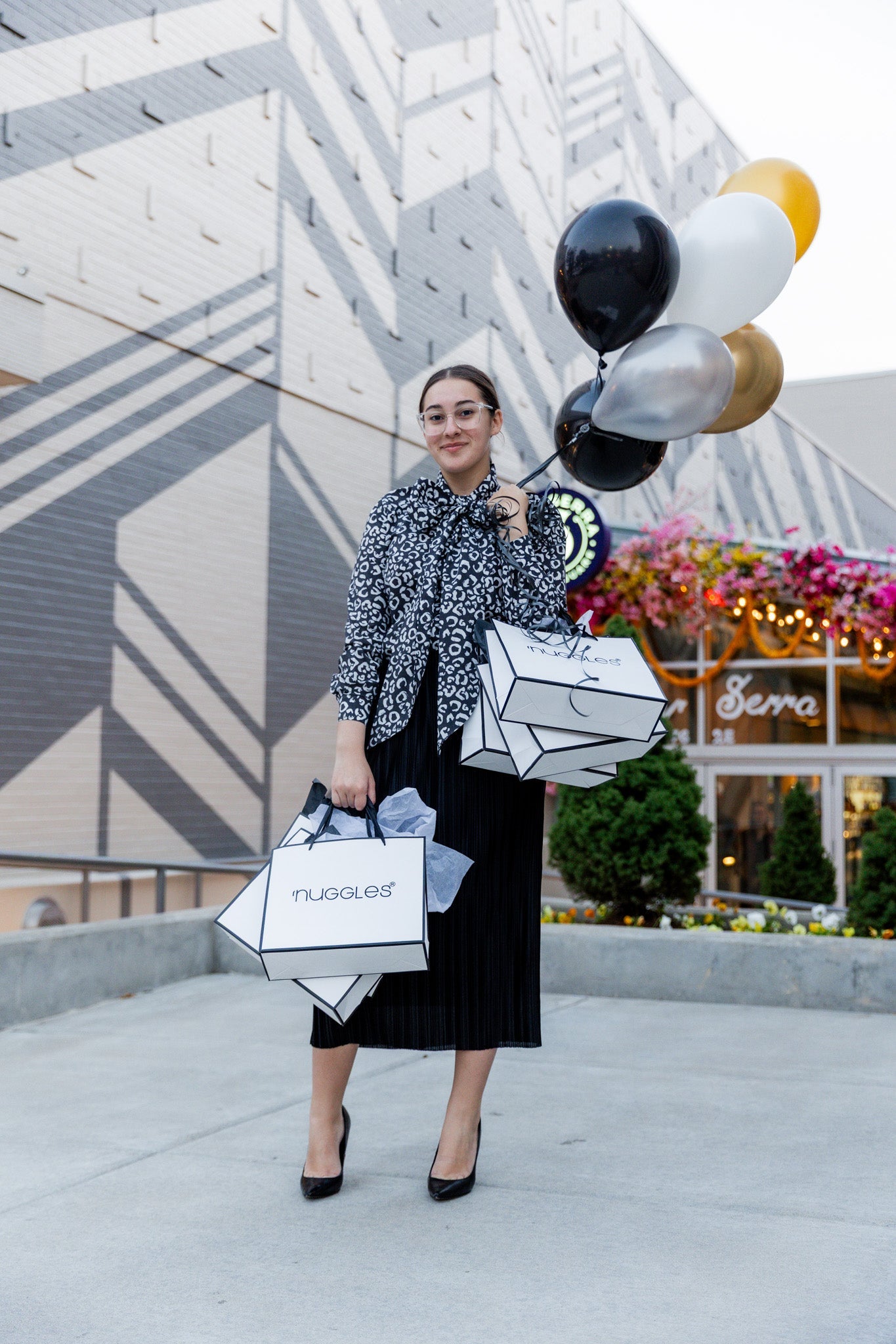 A Women holding black and gold balloons holding Nuggles® Shopping Bags celebrating the Black Friday Discounts.