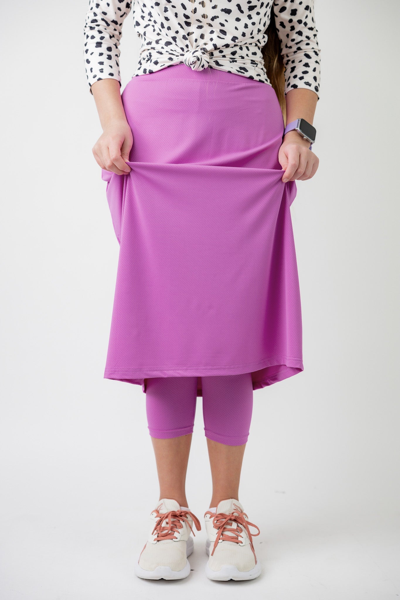 Woman wearing a bubblegum pink, modest athlete skirt with attached leggings. 