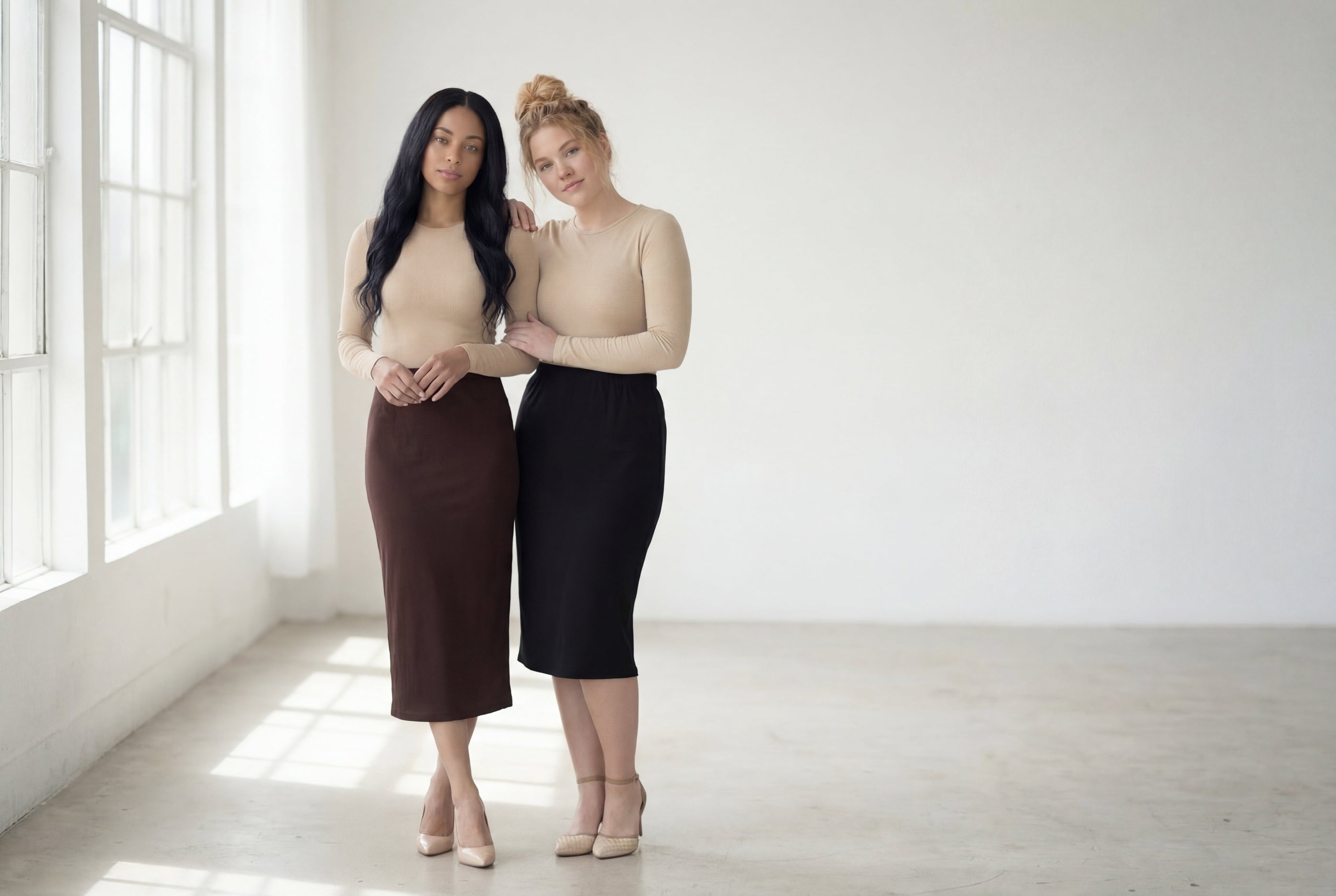 Two women standing in a minimal loft space wearing a black and brown modest skirt. 