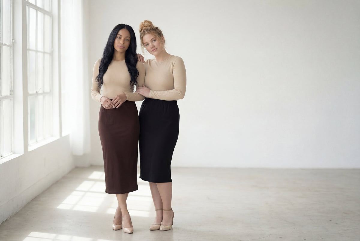 Two women standing in a minimal loft space wearing a black and brown modest skirt. 