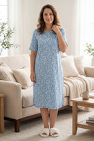 Woman wearing a blue floral dress standing in a living room.