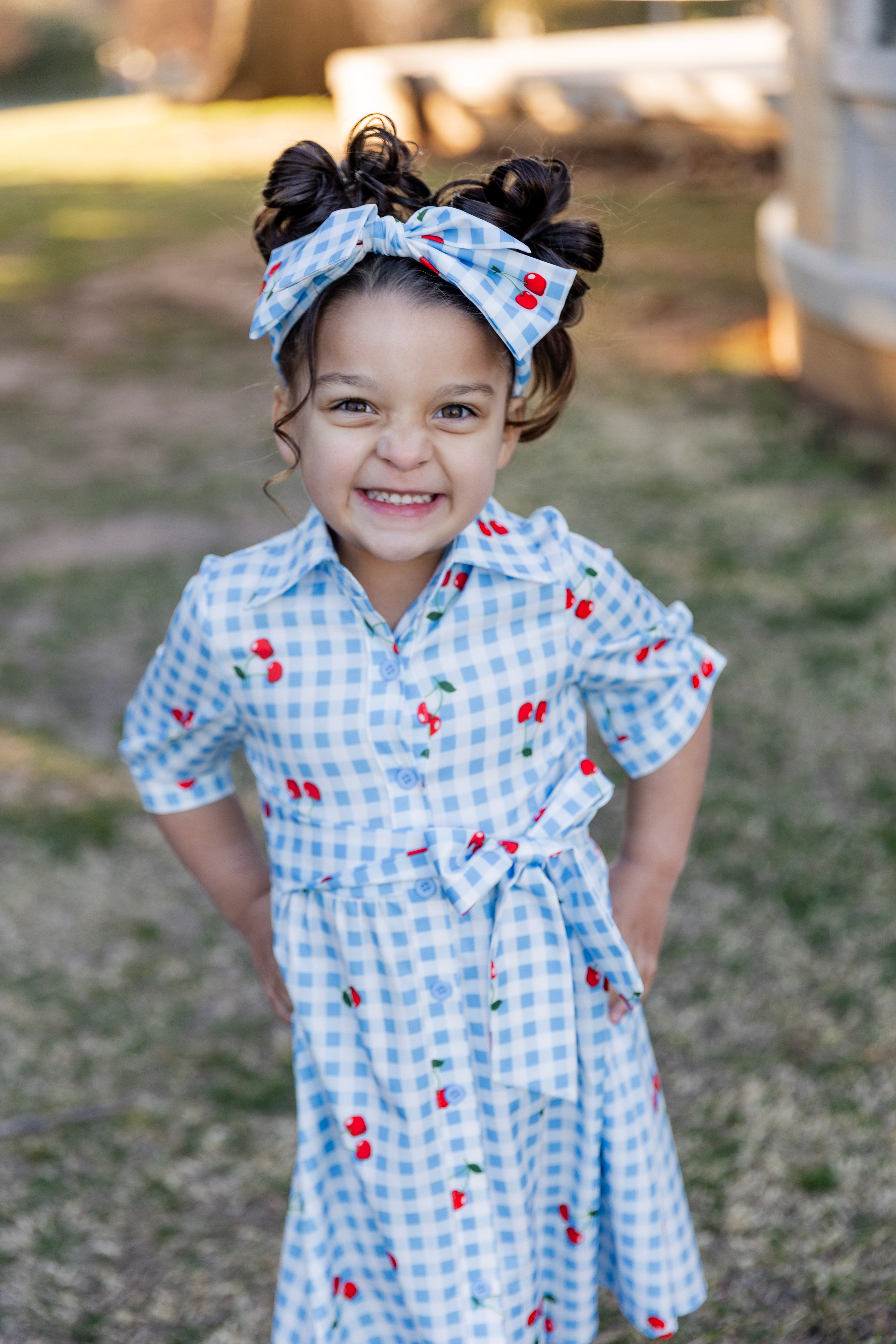 Model wearing the Nuggles® Girls' Rachel Dress and headband in Sweet Cherry Check