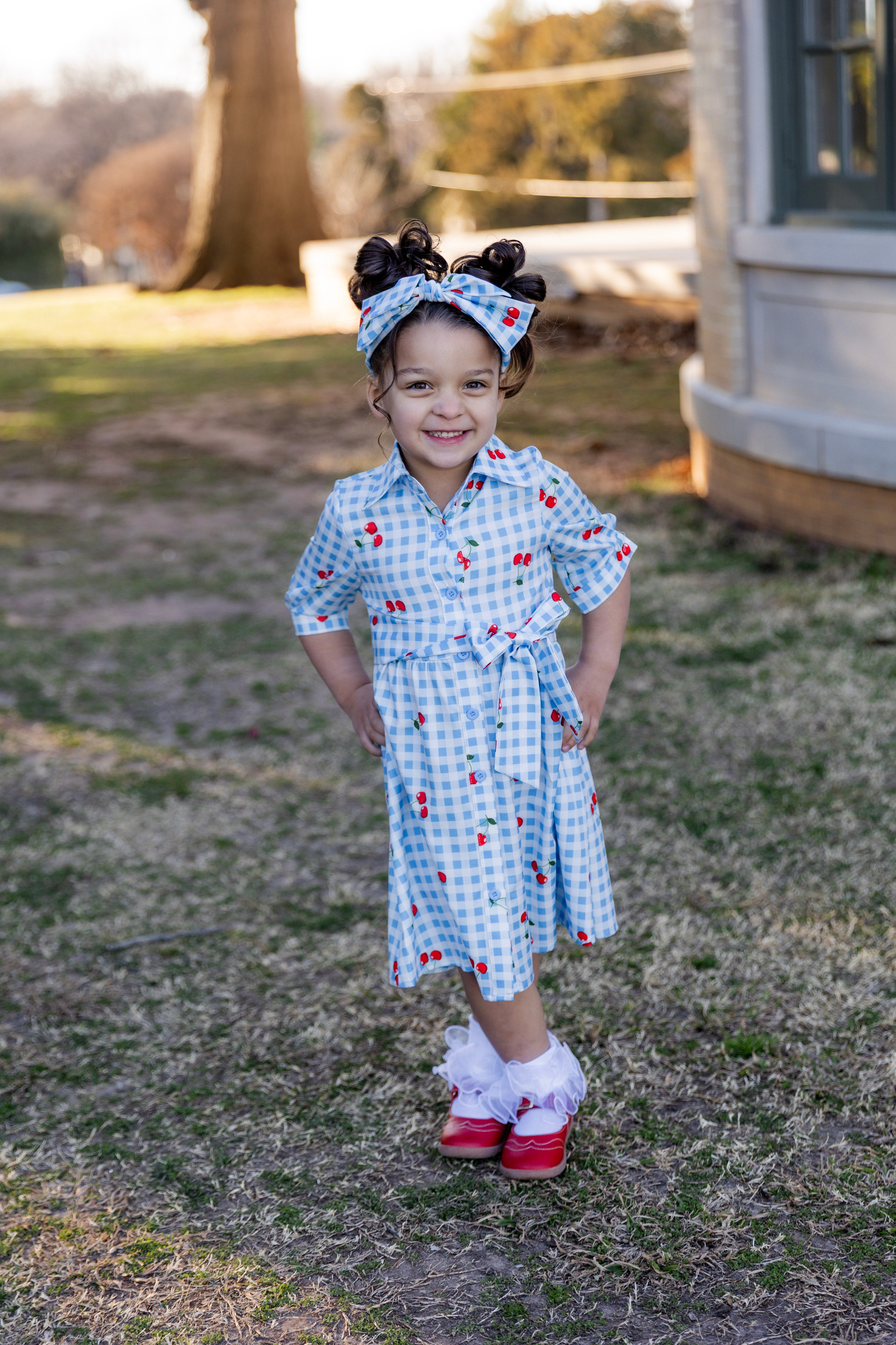 Model wearing the Nuggles® Girls' Rachel Dress and headband in Sweet Cherry Check