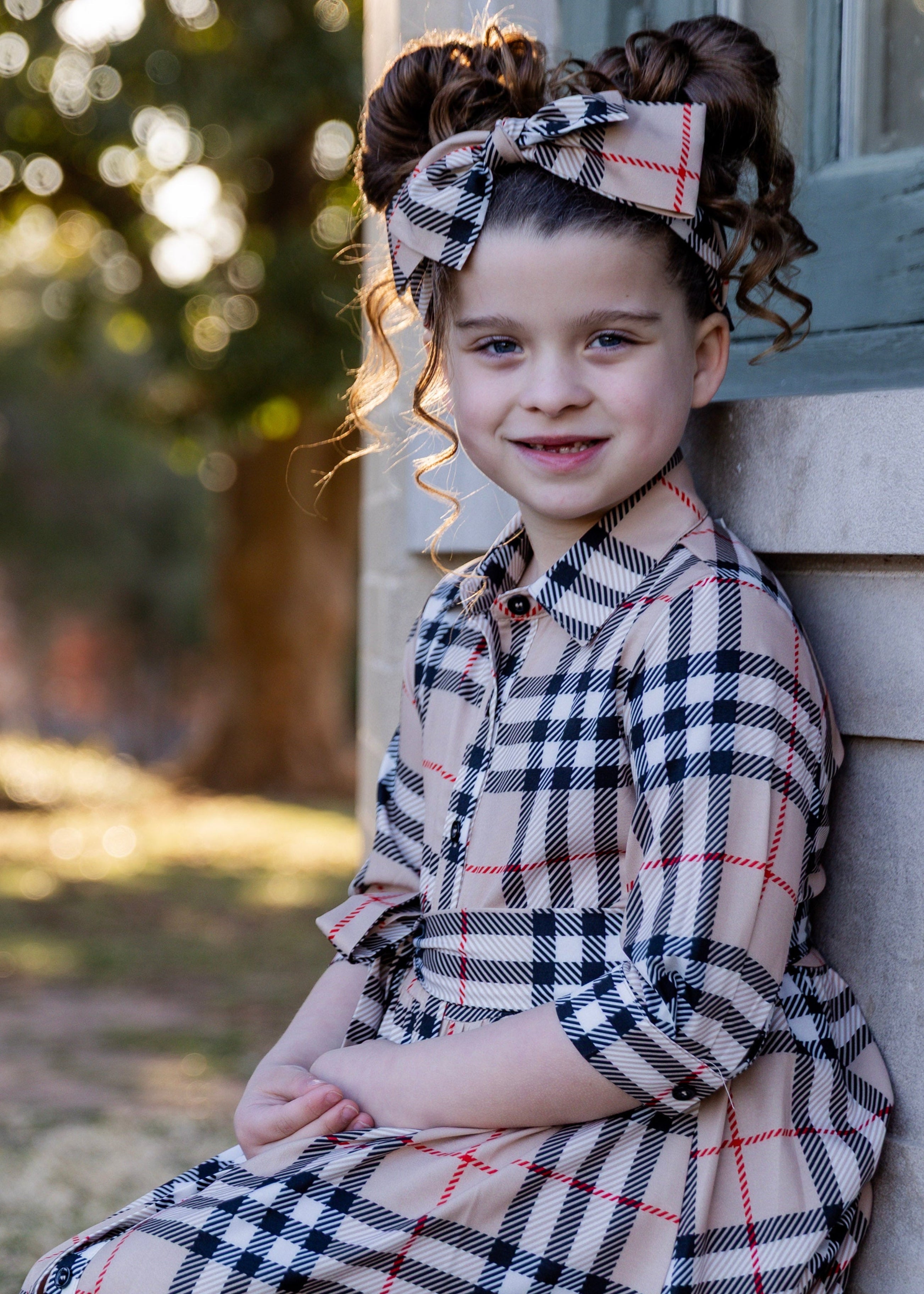 Model wearing the Nuggles® Girls' Rachel Dress and matching Headband in Sand Plaid