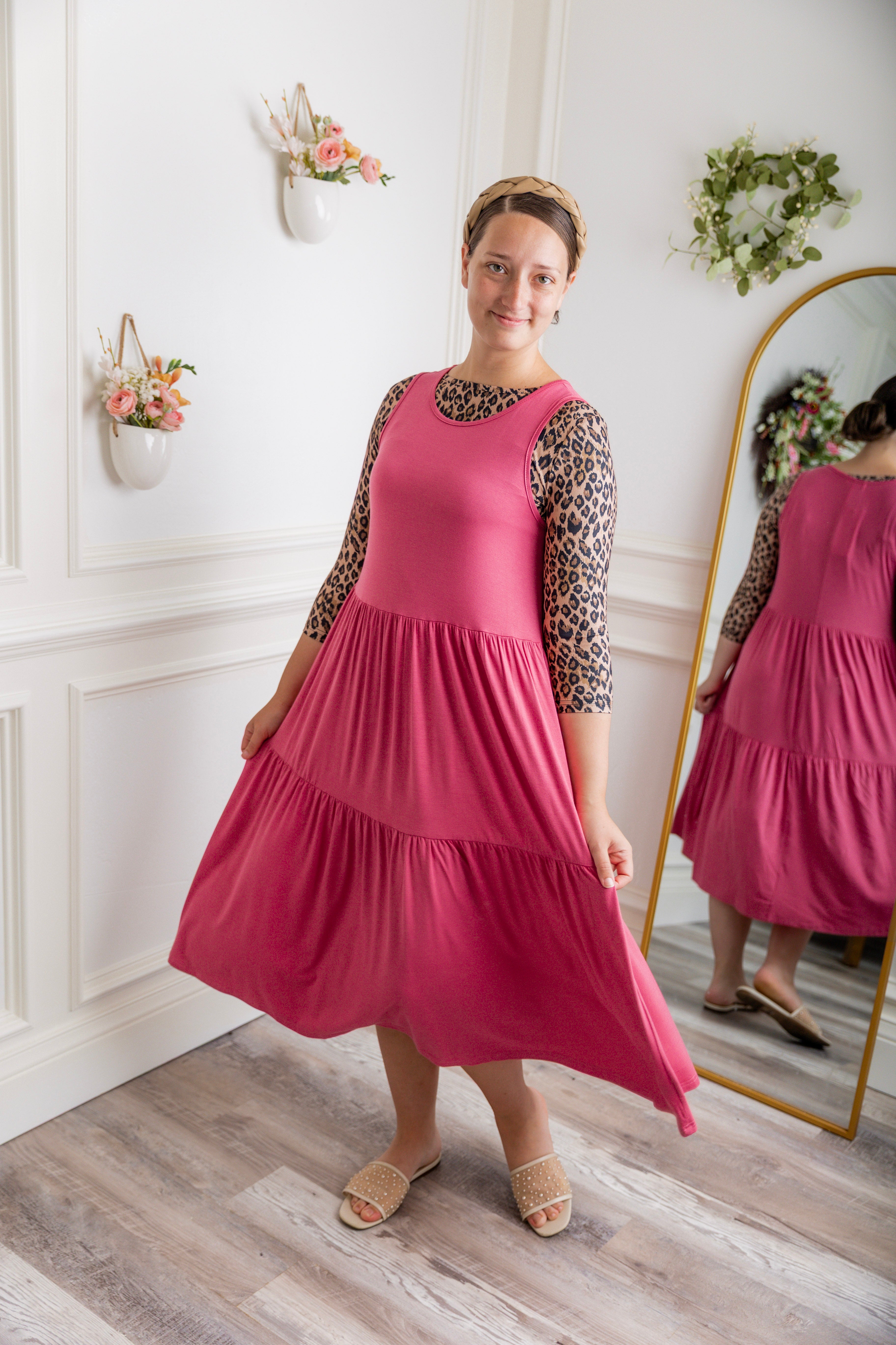 model modeling a pink tiered midi dress over a leopard print sleeve top, styled with nude studded sandals and a braided headband.