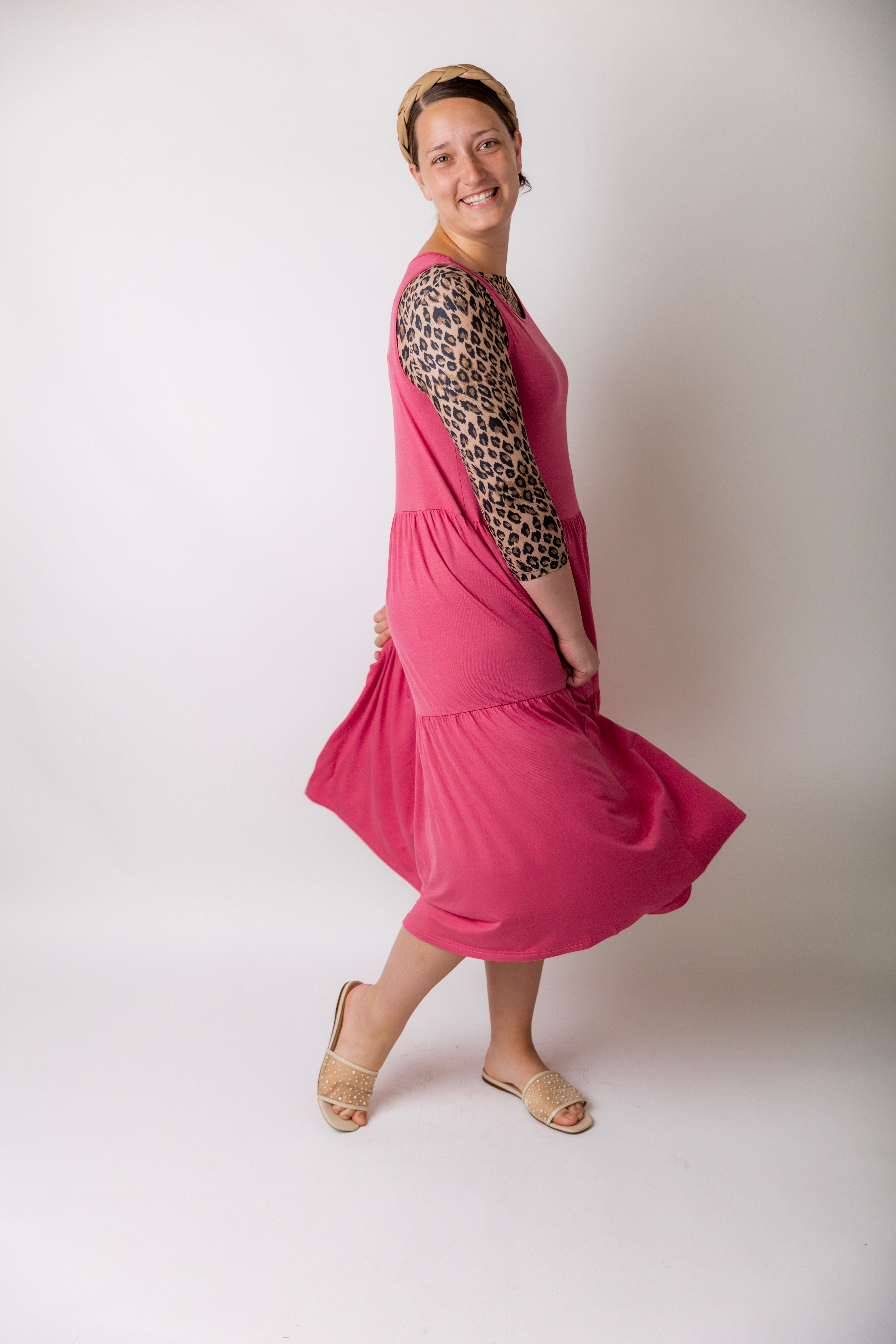 model modeling a pink tiered midi dress over a leopard print sleeve top, styled with nude studded sandals and a braided headband.