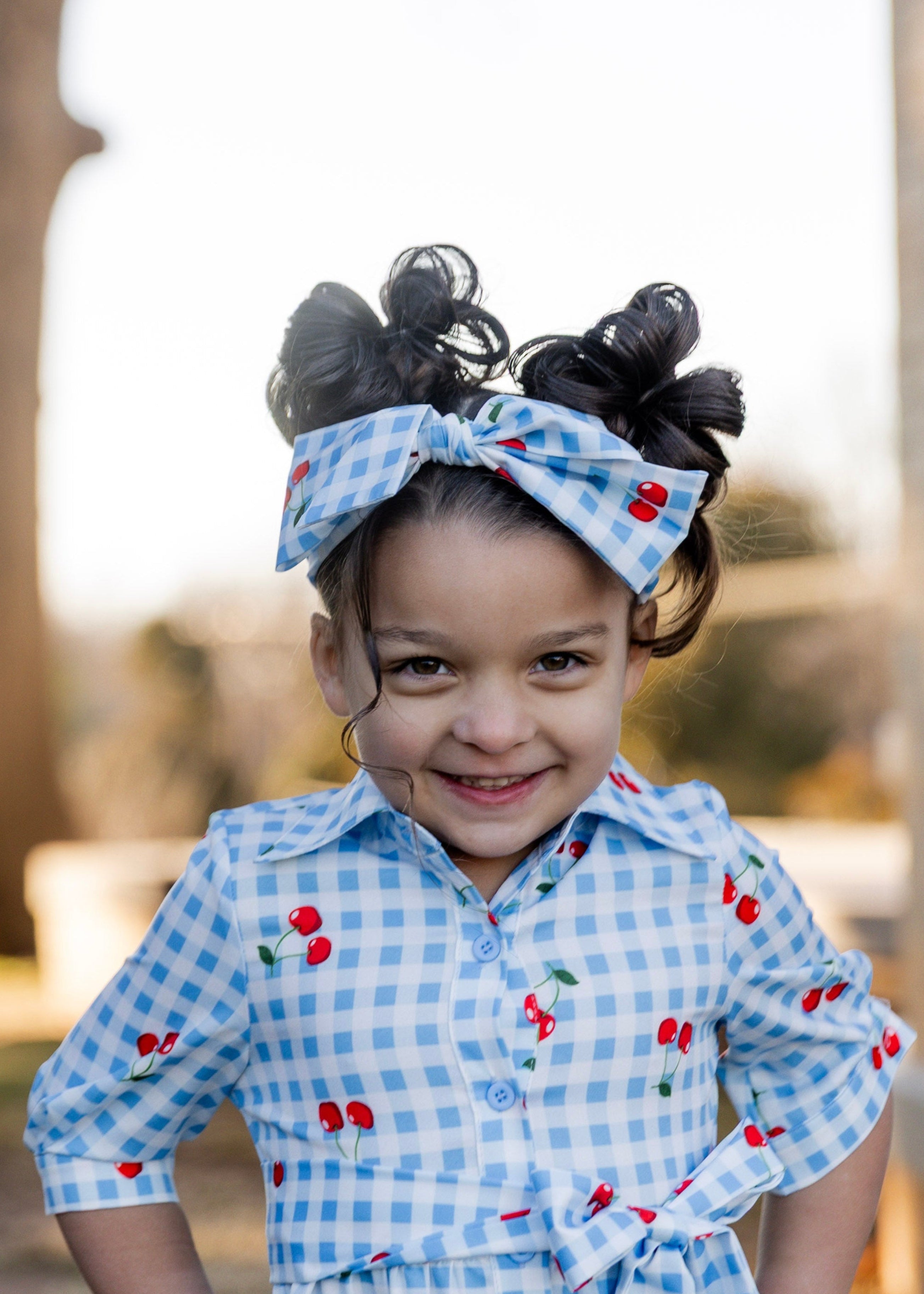 Model wearing the Nuggles® Girls' Rachel Dress and headband in Sweet Cherry Check
