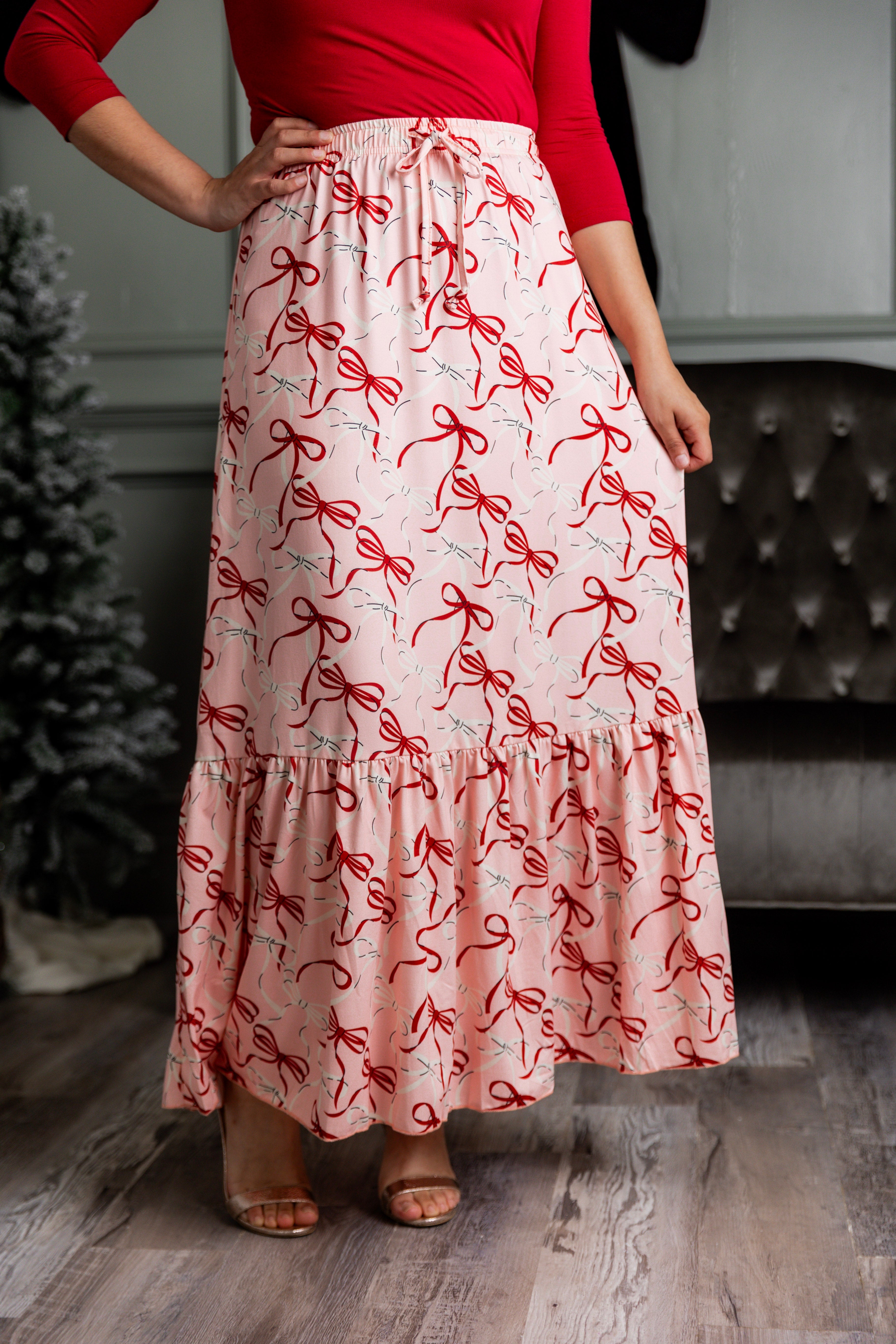 Model wearing the Nuggles® Sage Skirt in pink with red bow print, showcasing a tiered ruffle hem and soft, stretchy waistband.