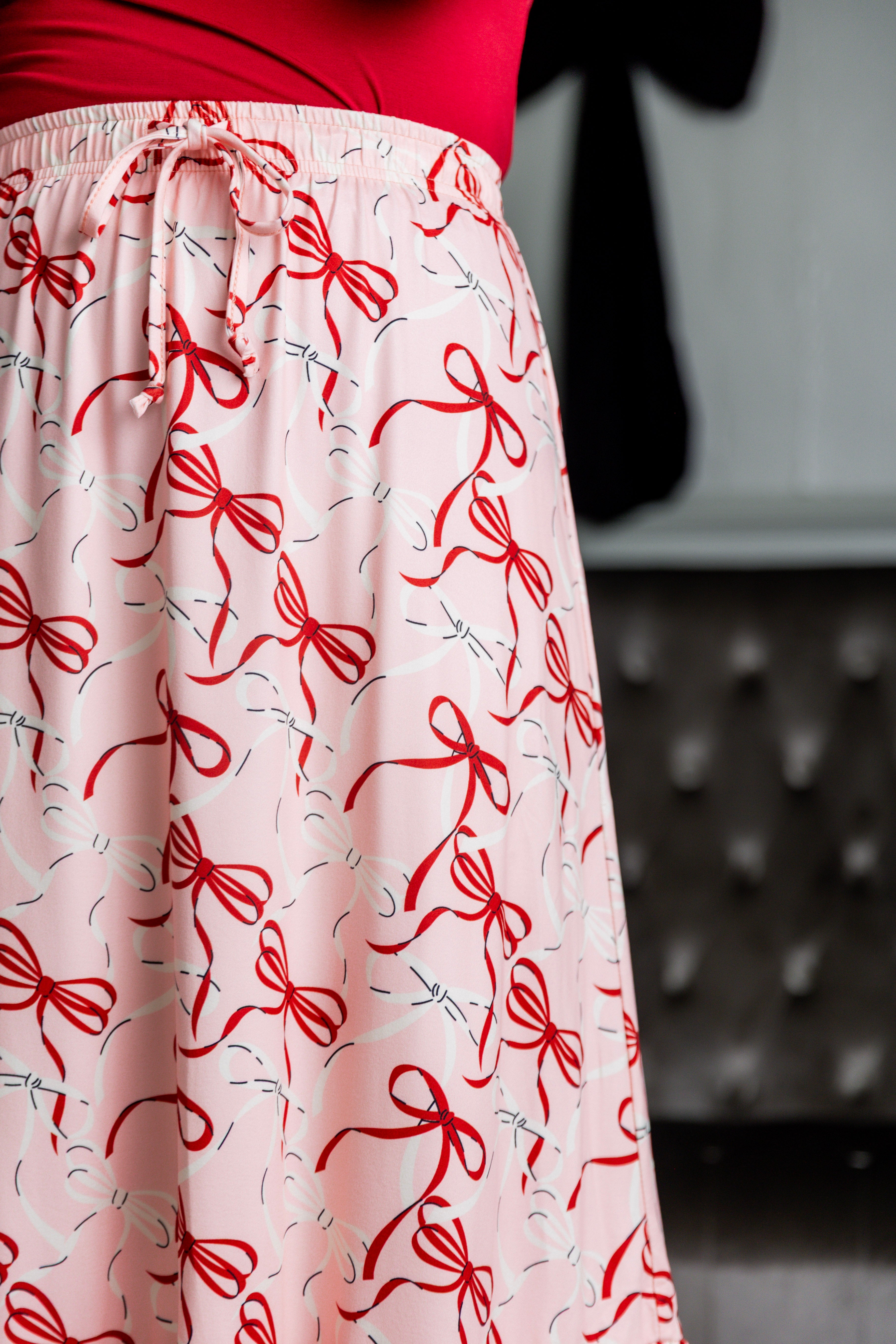 Model wearing the Nuggles® Sage Skirt in pink with red bow print, showcasing a tiered ruffle hem and soft, stretchy waistband.