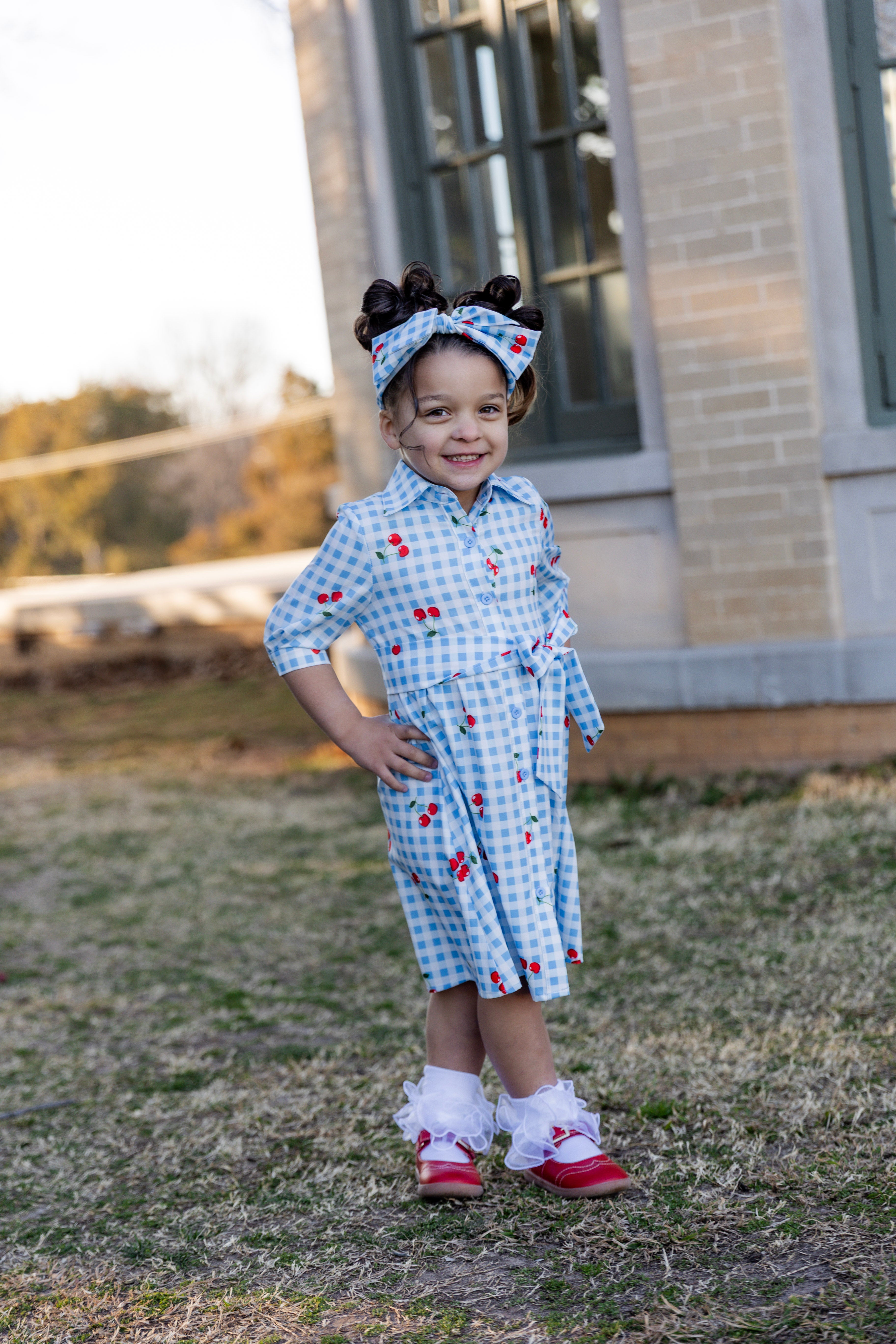 Model wearing the Nuggles® Girls' Rachel Dress and headband in Sweet Cherry Check