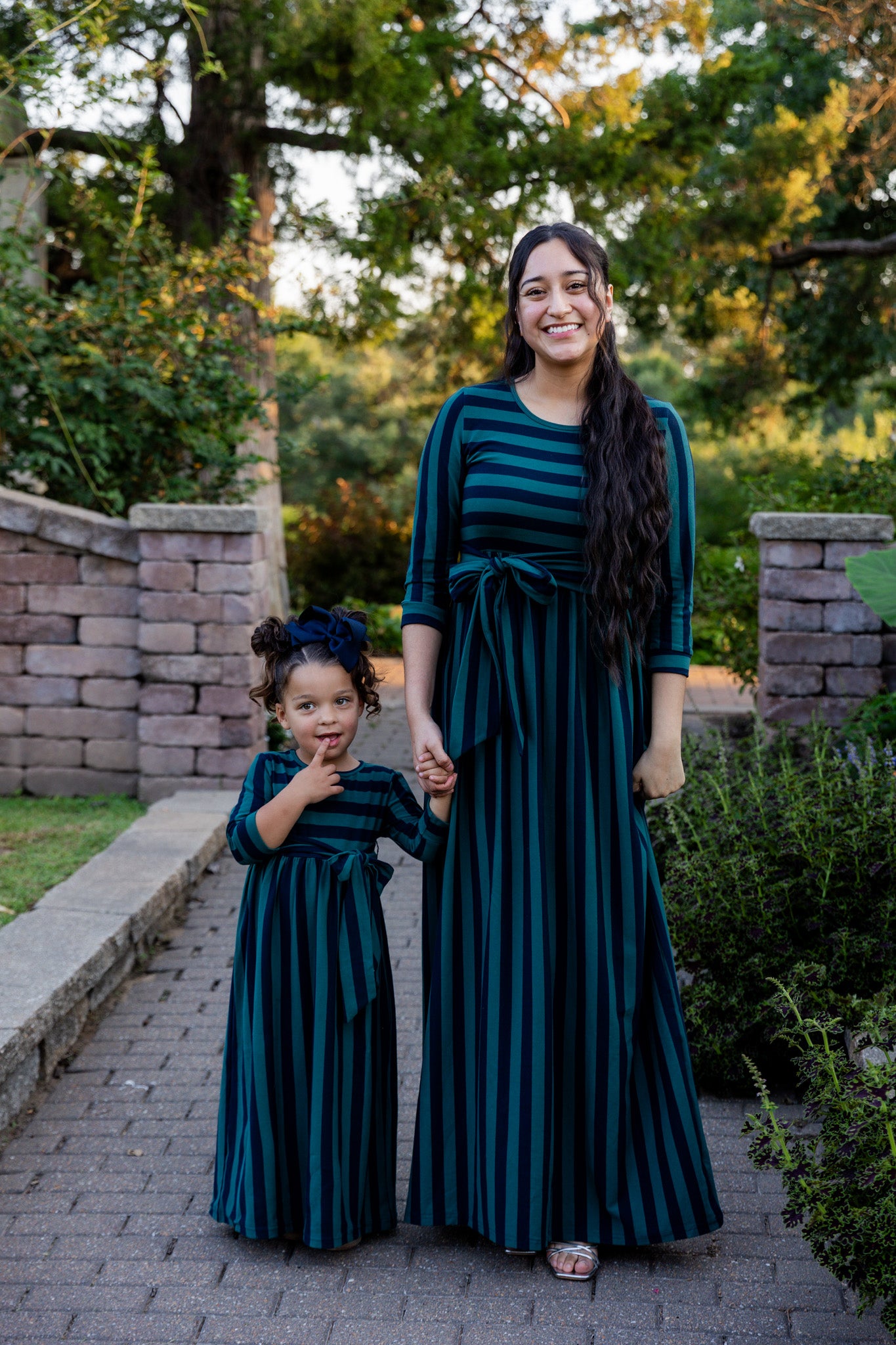 Young girl wearing the Nuggles® Girls Adelia Dress — a modest striped maxi dress with bow tie waist.