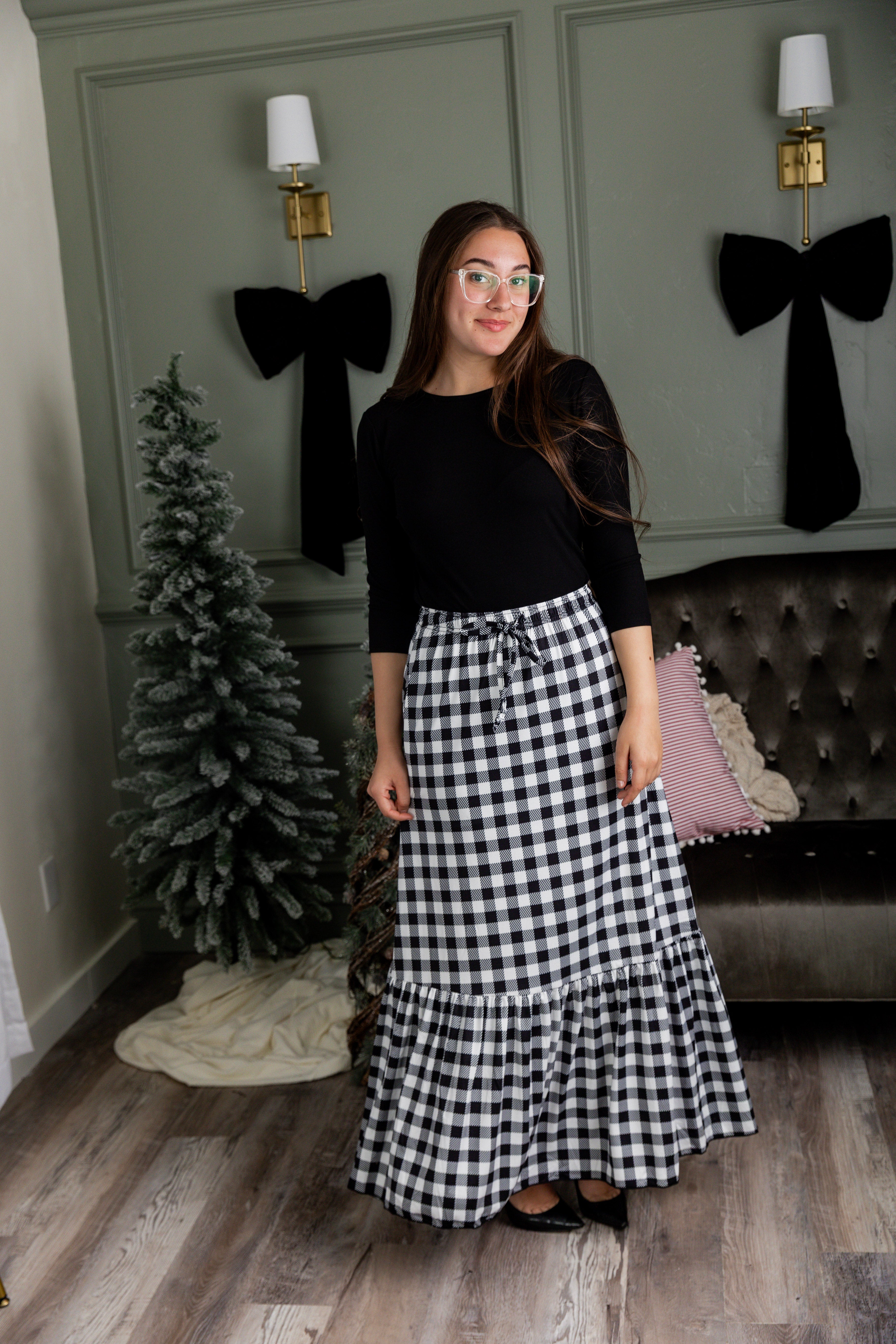 Model wearing the Nuggles® Sage Skirt in black and white gingham, featuring a tiered ruffle hem and drawstring waist.