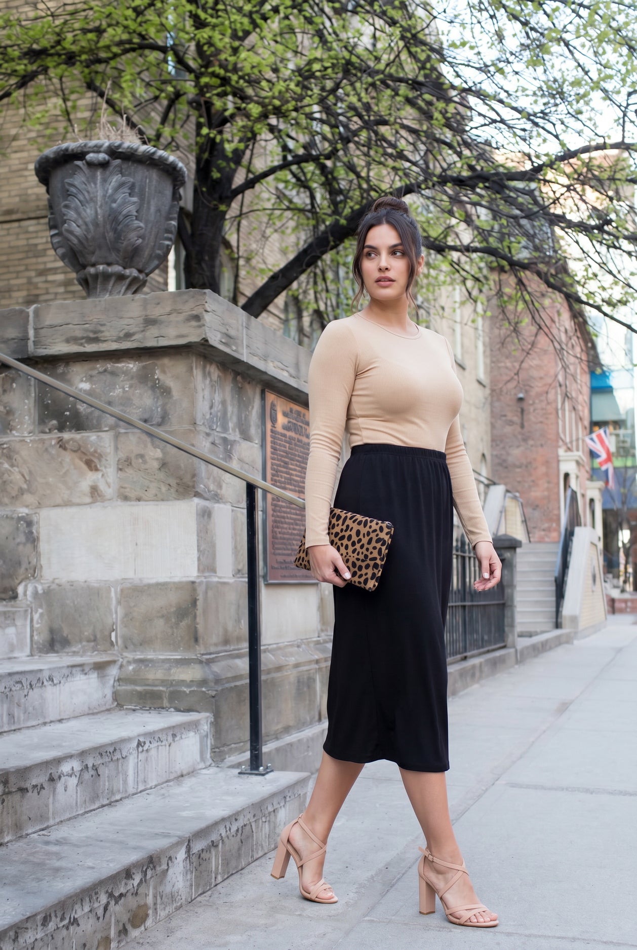 Woman in beige top and black skirt standing on a city street.
