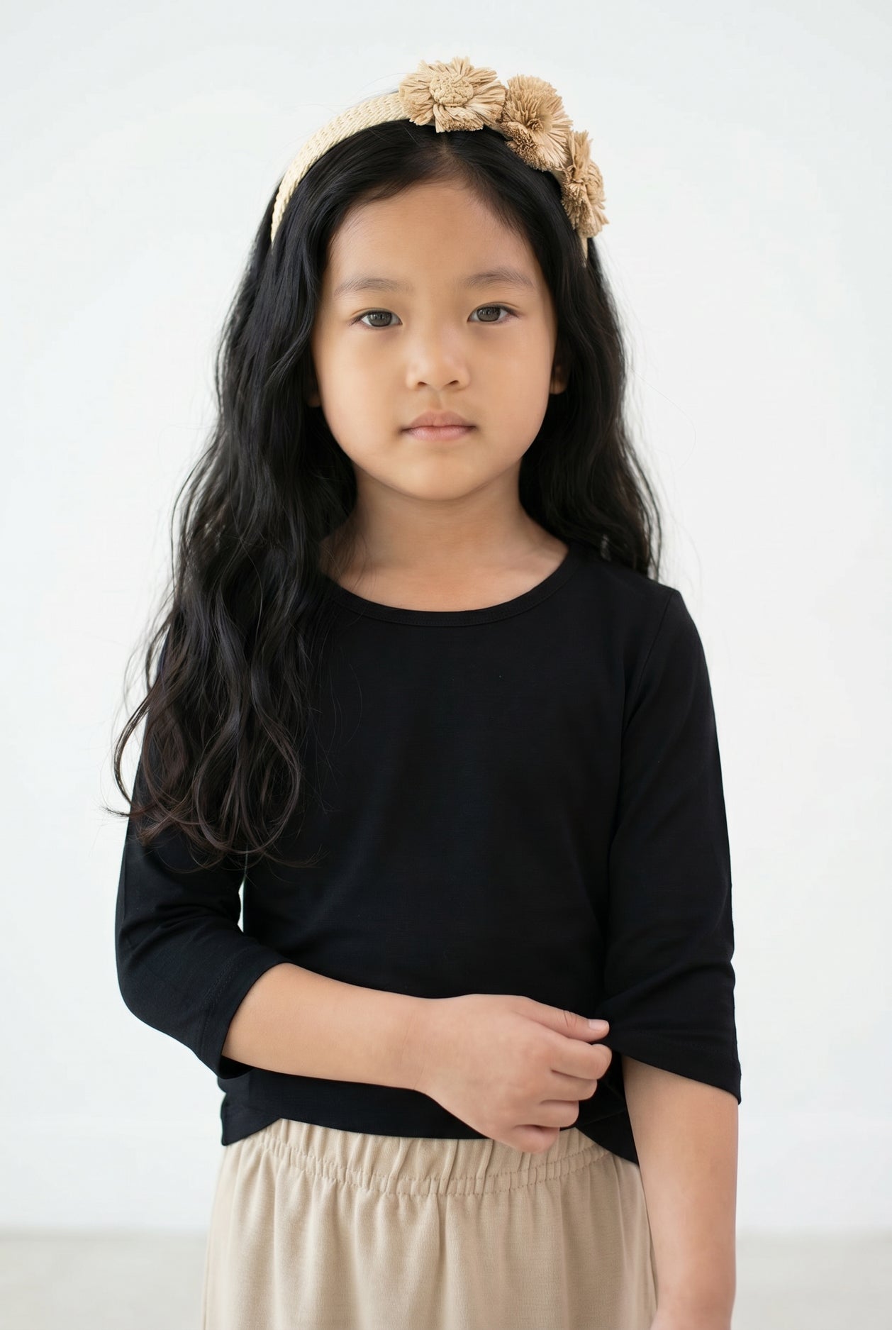 Young girl with long dark hair wearing Nuggles® Black Tee and a beige floral headband against a white background. 