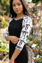 Person wearing a black and white patterned top standing in a garden with flowers and stone pillars.