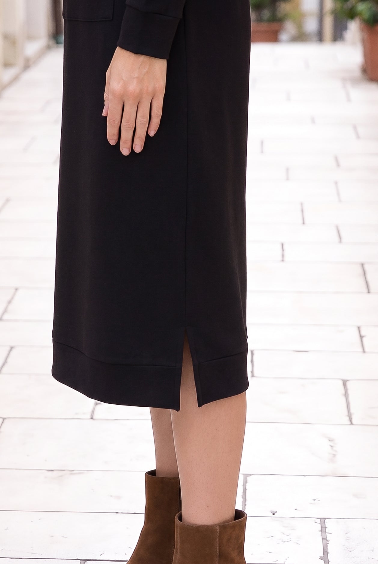 Nuggles® Oakley Hoodie Dress in Black, close-up of the banded hem and side slit with brown suede ankle boots