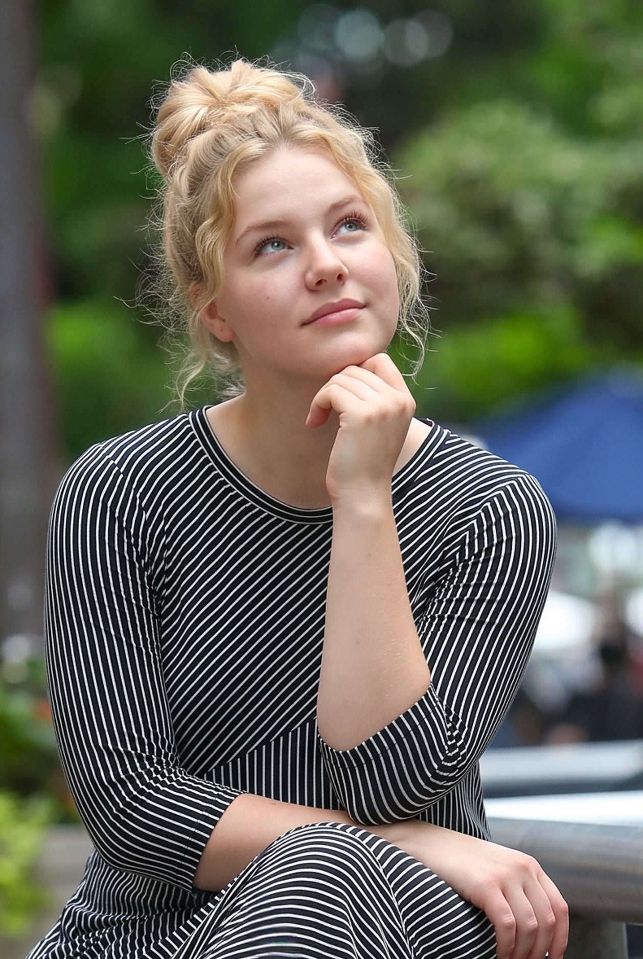 Woman in a striped dress sitting outdoors with trees in the background