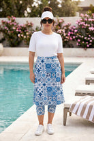 Woman wearing a white top and blue patterned skirt by a poolside.