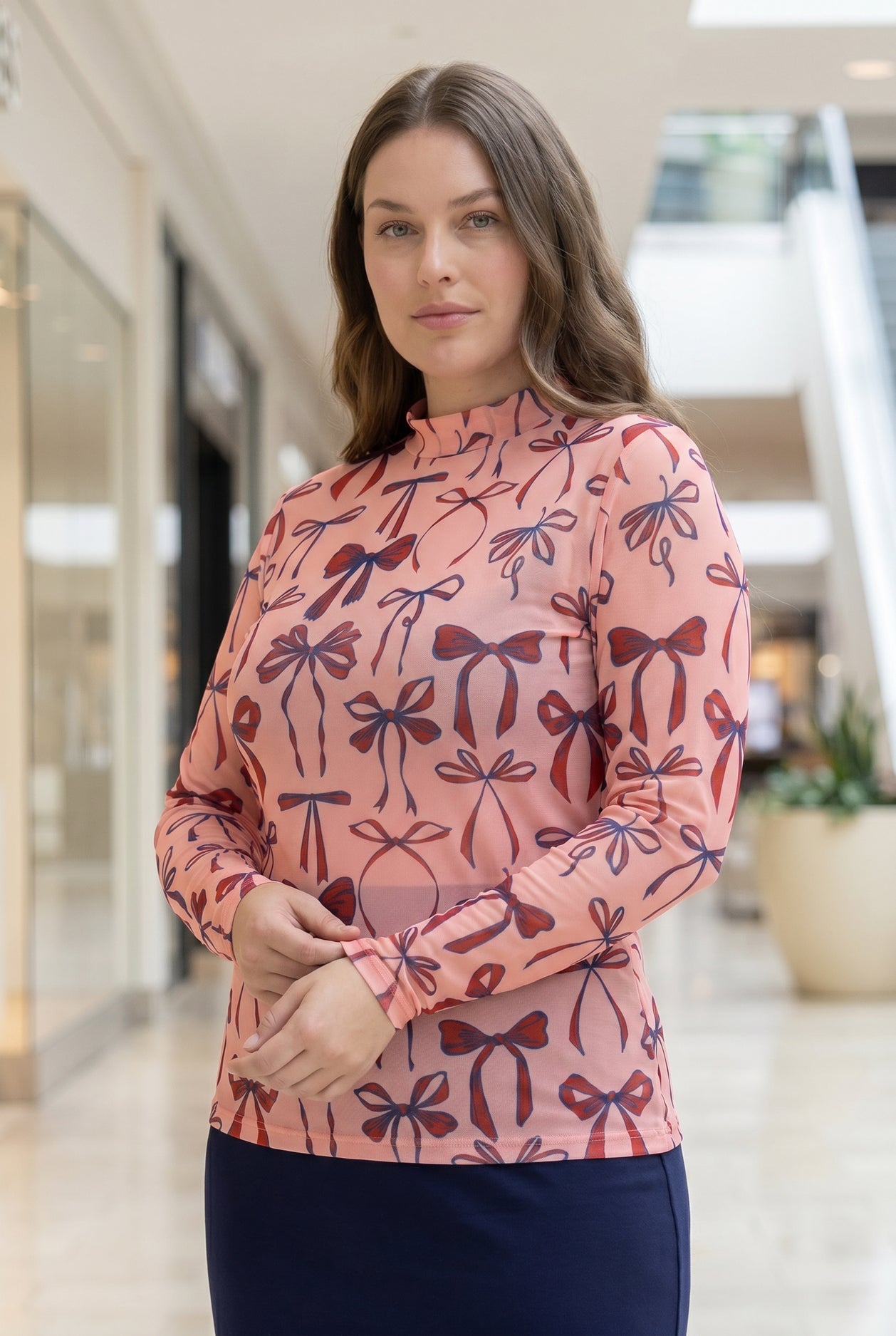 A picture of a women wearing a pink, red, and blue bow print mesh tee. 