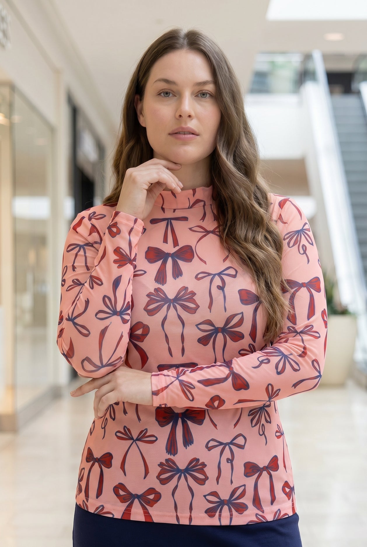A picture of a women wearing a pink, red, and blue bow print mesh tee. 