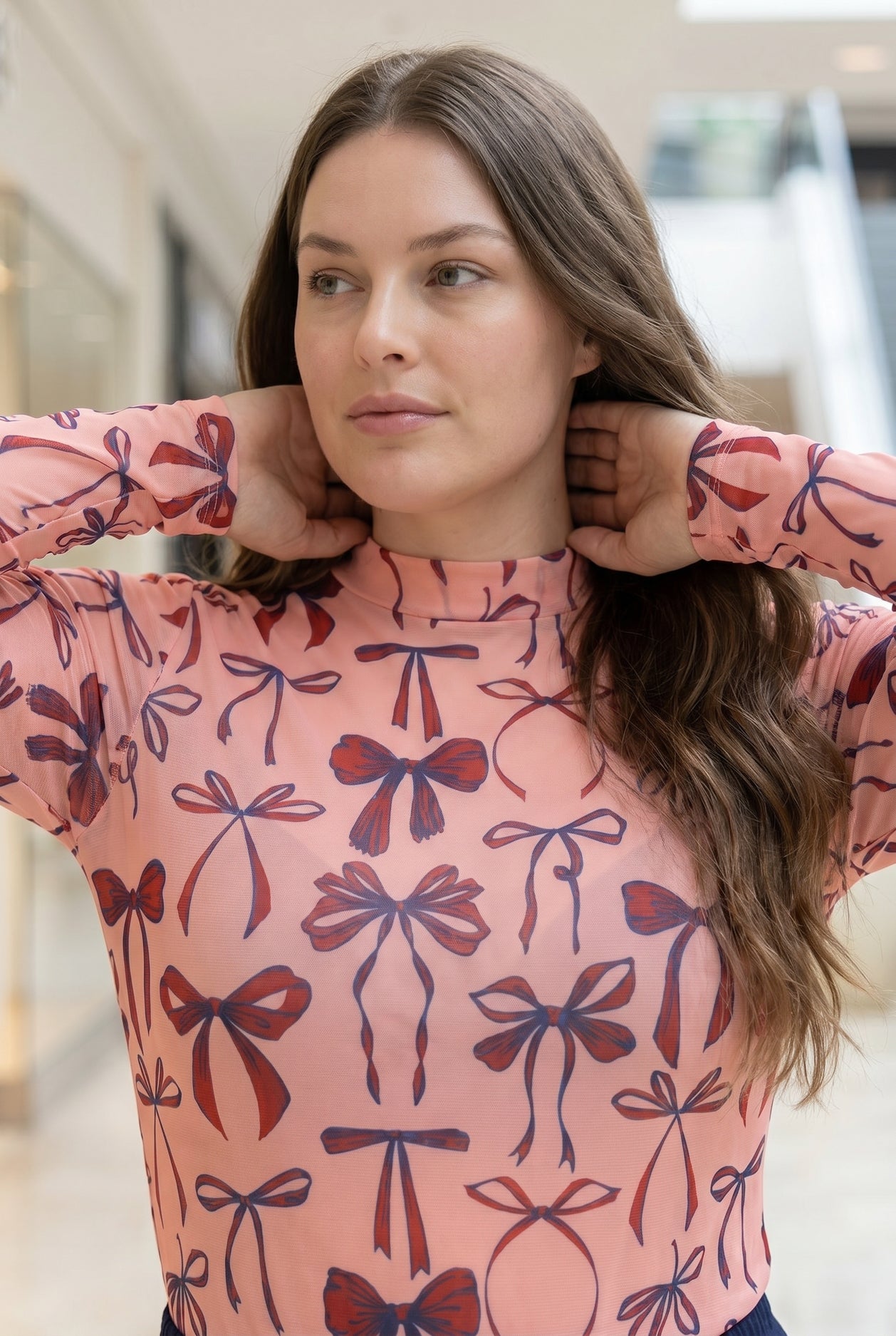 A picture of a women wearing a pink, red, and blue bow print mesh tee. 