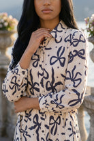 A picture of a young women wearing the Leila Dress in a bow print with a soft ivory base. 