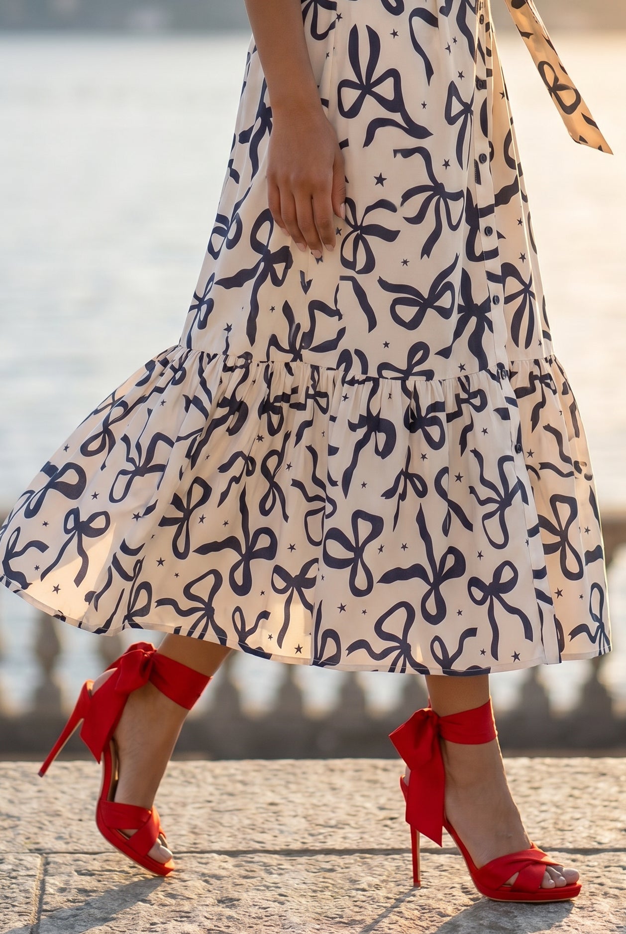 A picture of a young women wearing the Leila Dress in a bow print with a soft ivory base. 