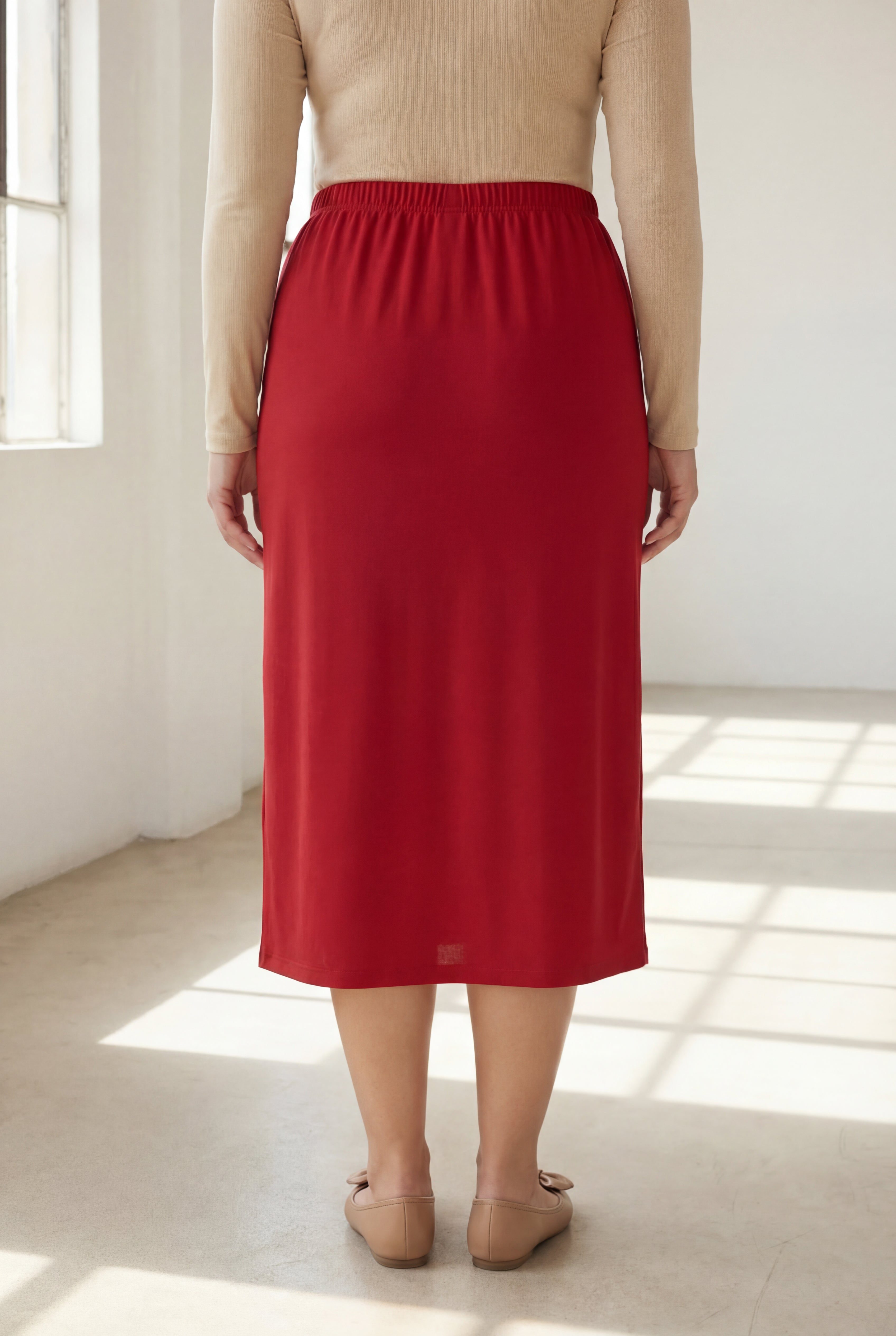Person wearing a red skirt in a bright room with sunlight filtering through.