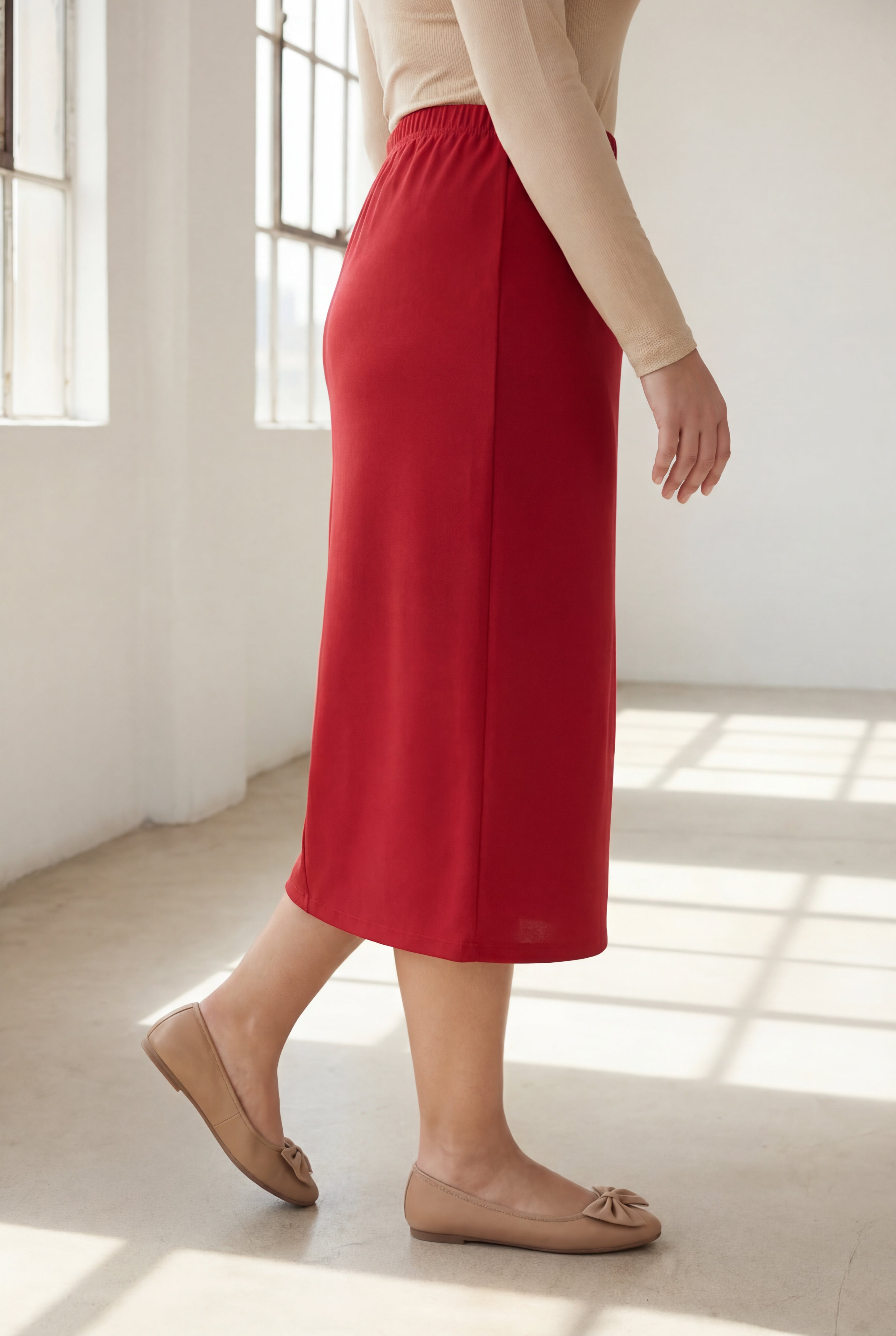 Person wearing a red skirt and beige top in a bright room with sunlight filtering through.