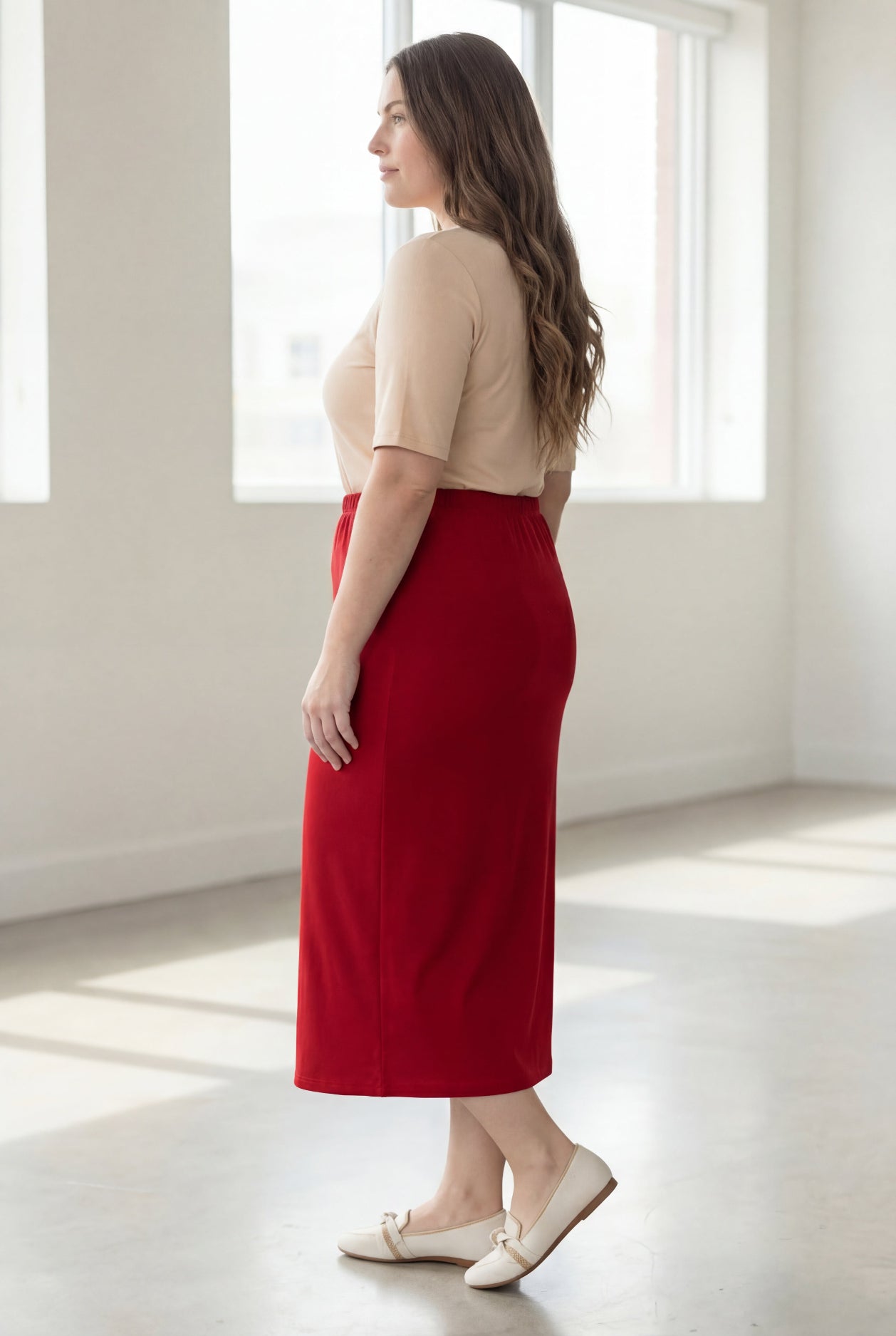 Woman wearing a red skirt and beige top in a bright room with large windows.