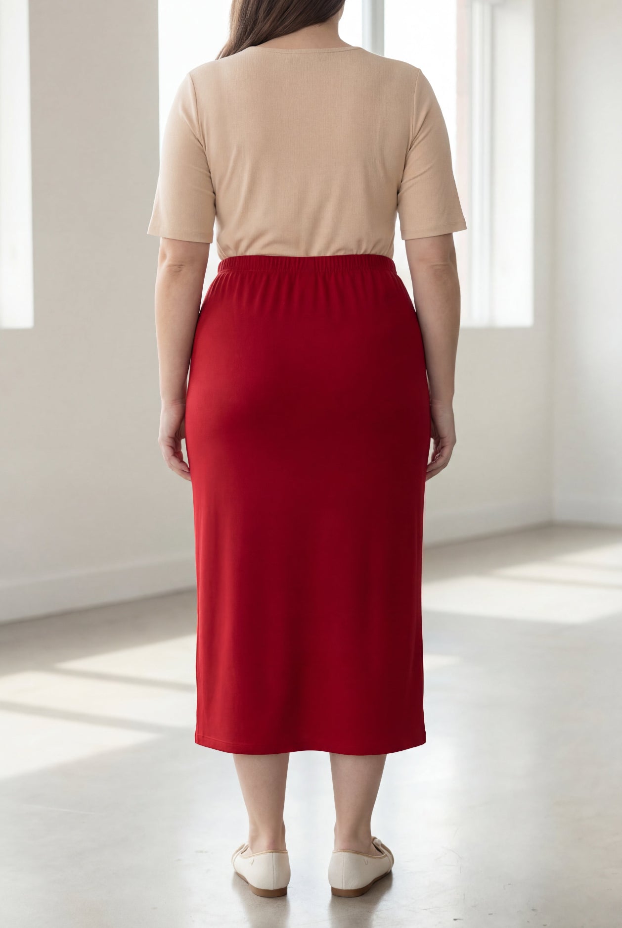 Person wearing a beige top and red skirt in a bright room.