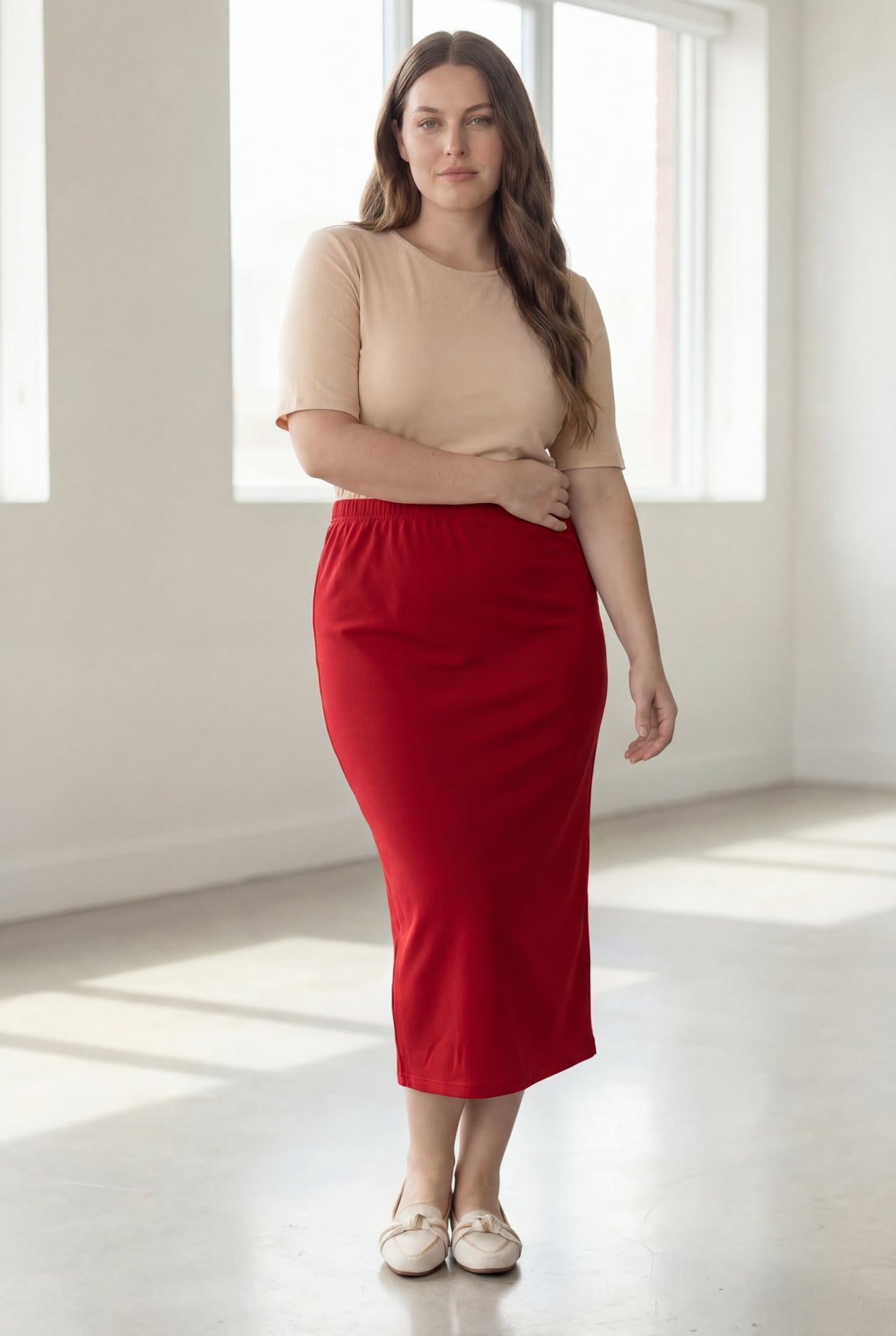 Woman wearing a beige top and red skirt in a bright room.