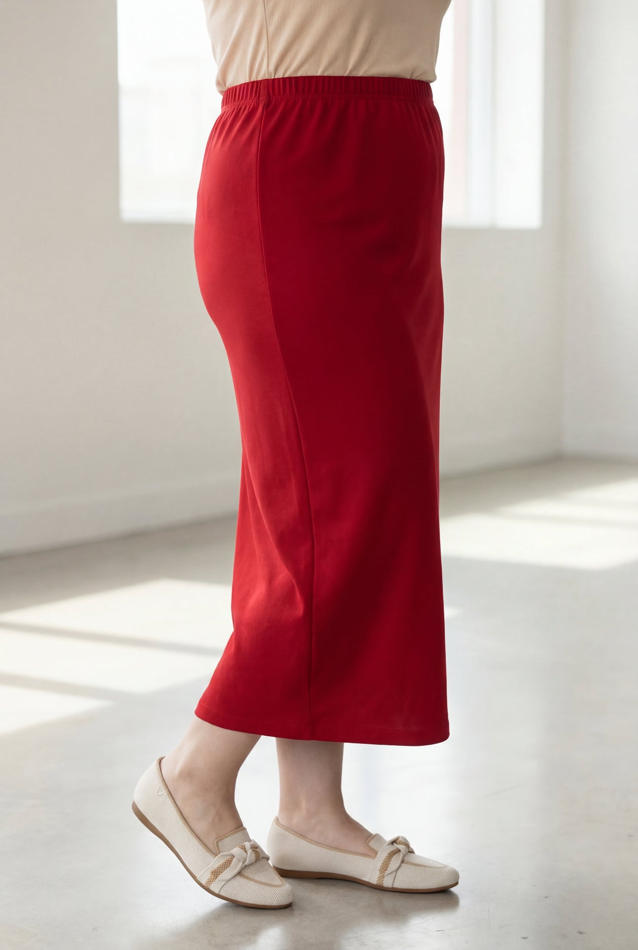 Person wearing a red skirt and white shoes in a bright room