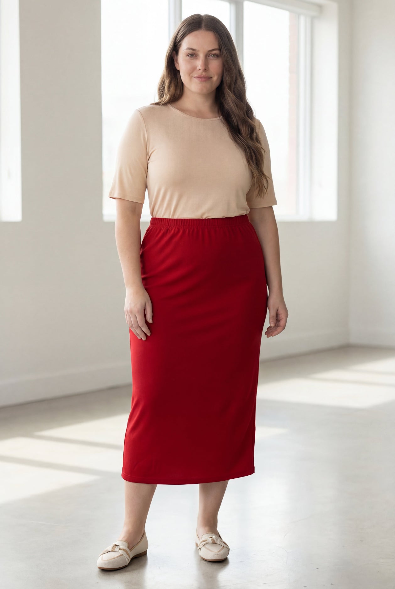 Woman wearing a beige top and red skirt in a bright room.