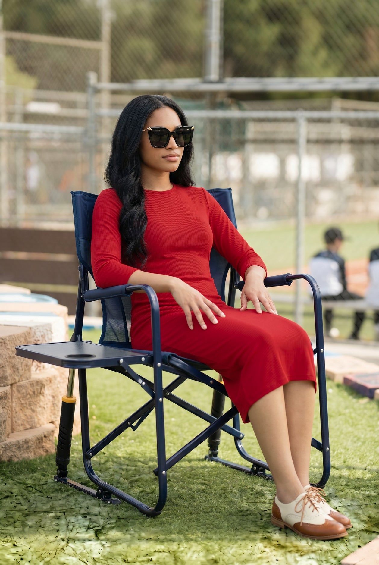 Woman in a red dress sitting on a folding chair outdoors.