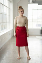 Women wearing a brick red classic 27" midi length skirt with a beige shirt in a sunlight loft.