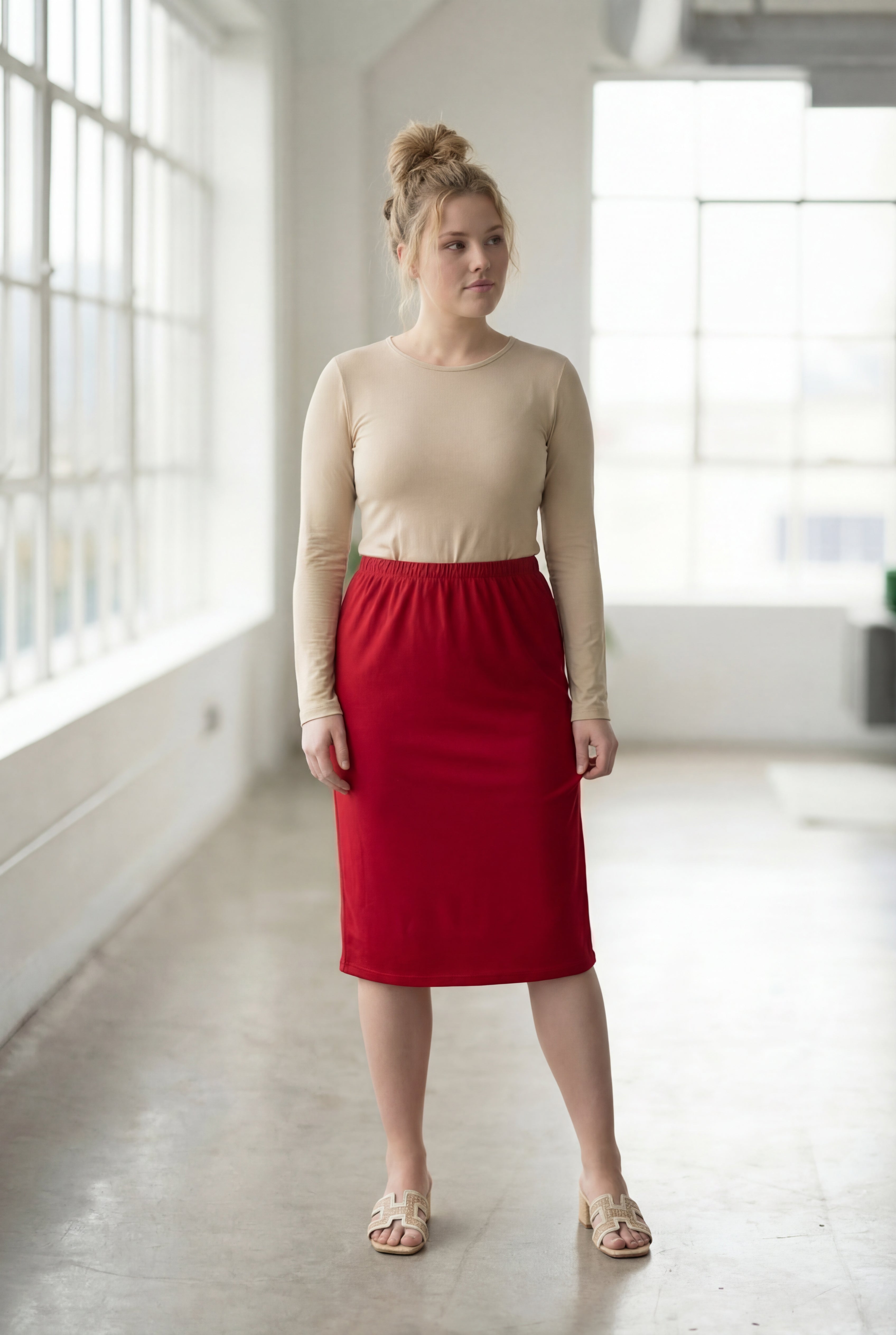 Women wearing a brick red classic 27" midi length skirt with a beige shirt in a sunlight loft.