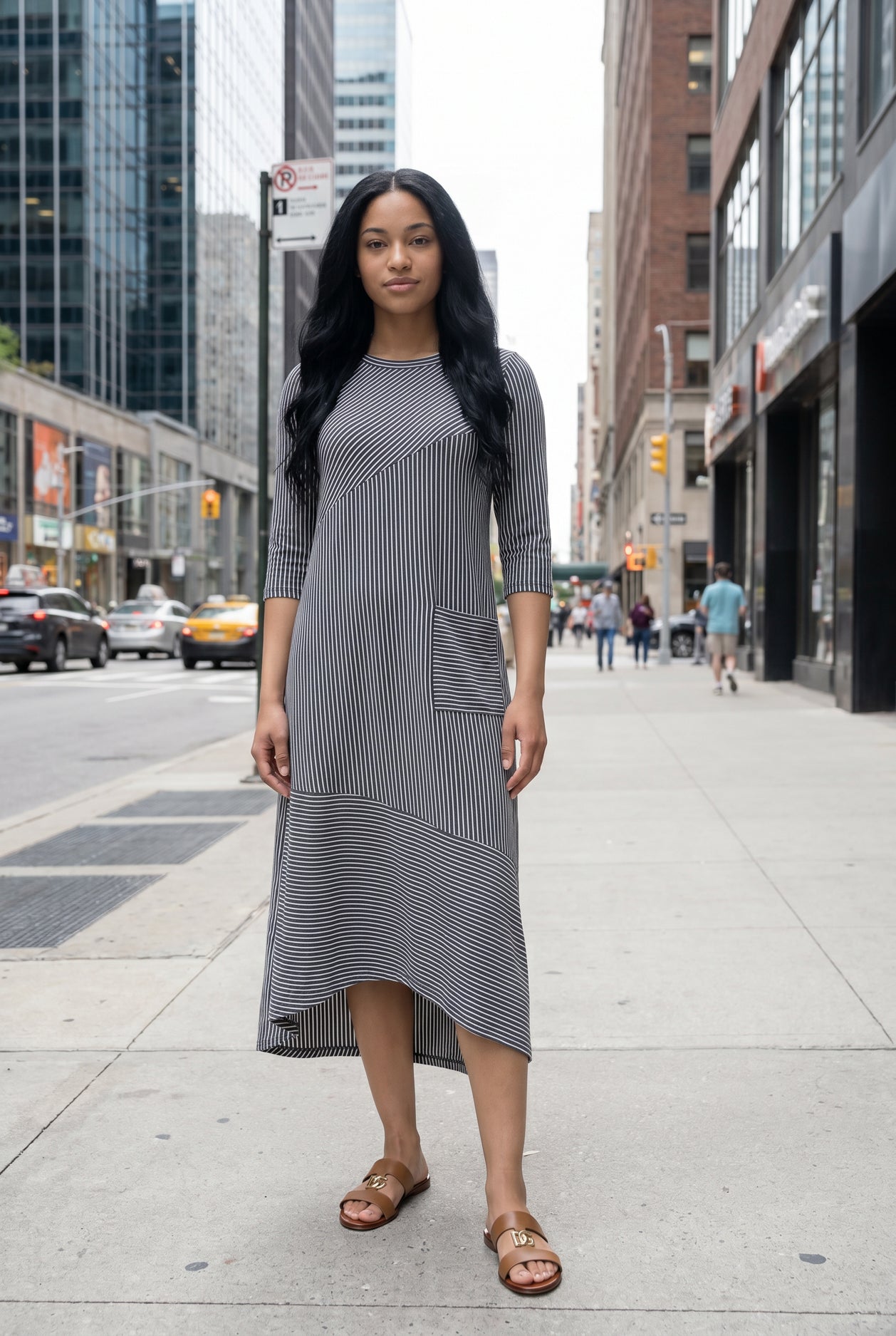 Woman in a gray dress standing on a city street with tall buildings in the background.
