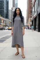 Woman in a gray dress standing on a city street with tall buildings in the background.