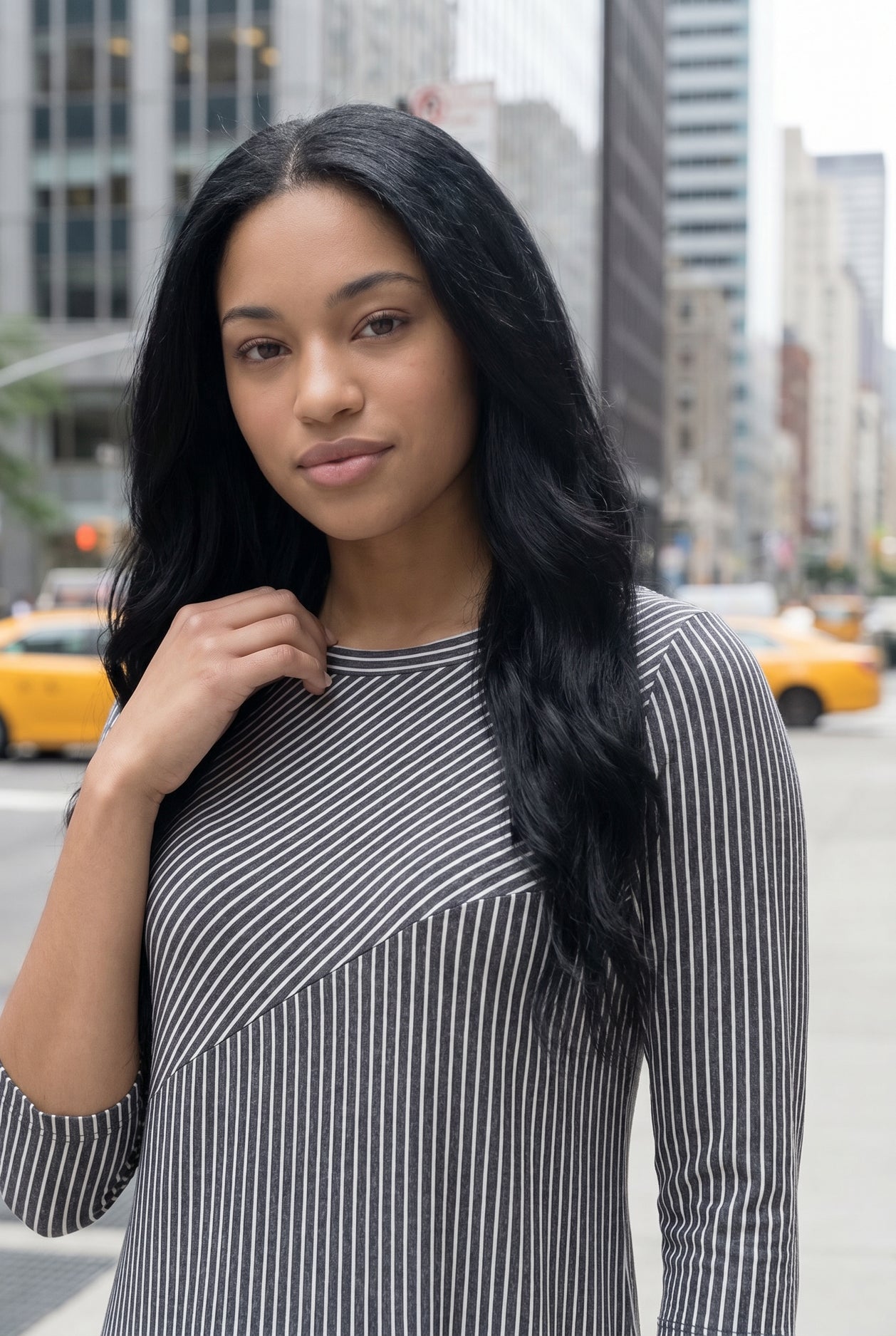 Woman in a gray dress standing on a city street with tall buildings in the background.