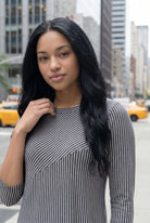 Woman in a gray dress standing on a city street with tall buildings in the background.