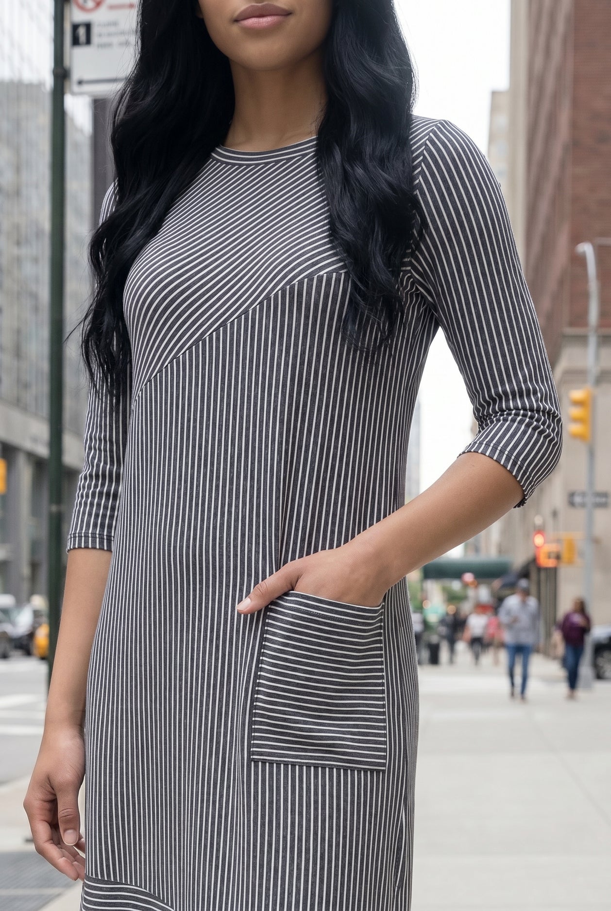 Woman in a gray dress standing on a city street with tall buildings in the background.