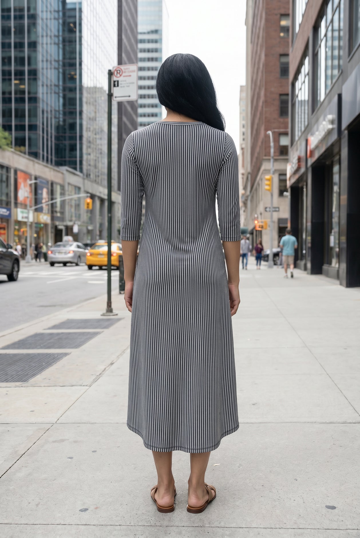 Woman in a gray dress standing on a city street with tall buildings in the background.