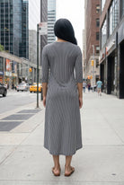 Woman in a gray dress standing on a city street with tall buildings in the background.