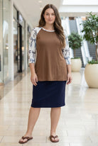 Woman modeling a chestnut brown top with white ribbon-print sleeves and a navy skirt in a bright indoor shopping mall setting.