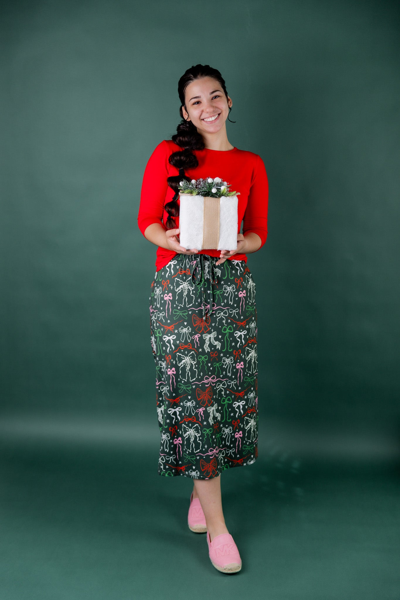 Woman holding a gift box with a green background wearing a nuggles holiday themed sport skirt.