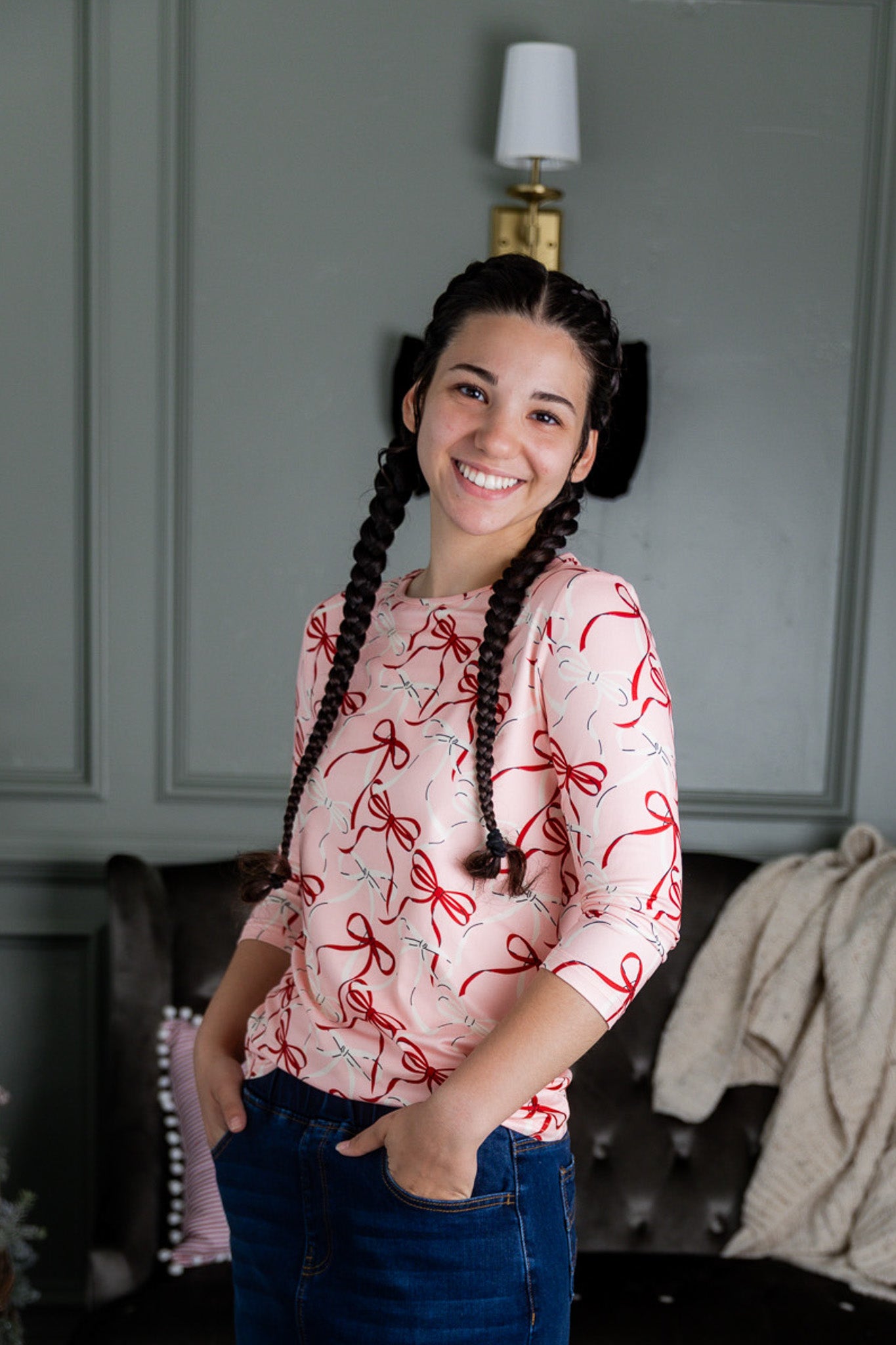 Woman with braided hair wearing a pink shirt with red patterns in a room.