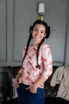 Woman with braided hair wearing a pink shirt with red patterns in a room.