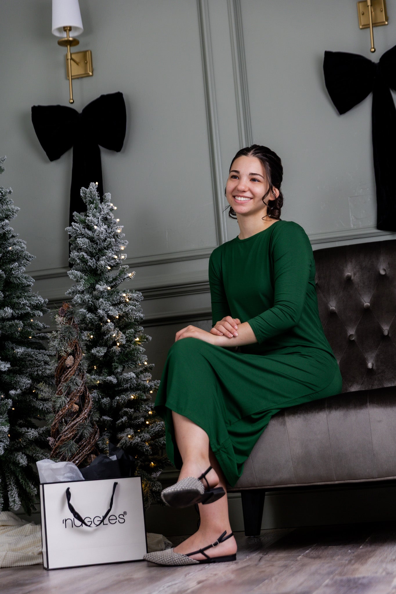 Woman in a green layering dress sitting on a couch with decorative Christmas trees and a Nuggles bag in the background.