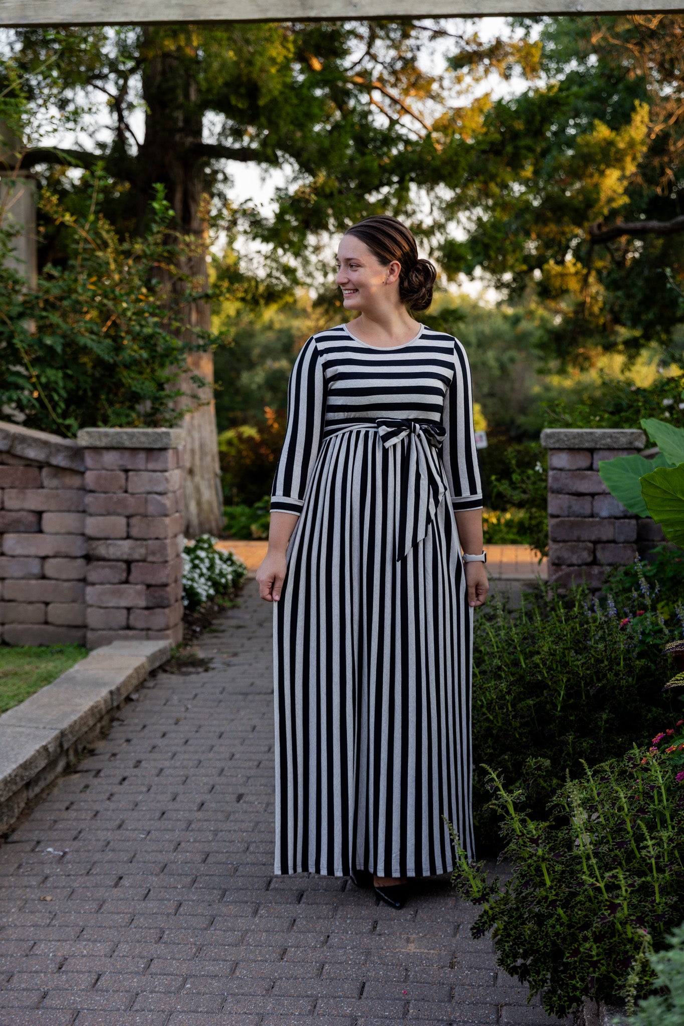 Model wearing the Nuggles® Adelia Dress, a modest striped maxi dress with waist tie and ¾ sleeves.